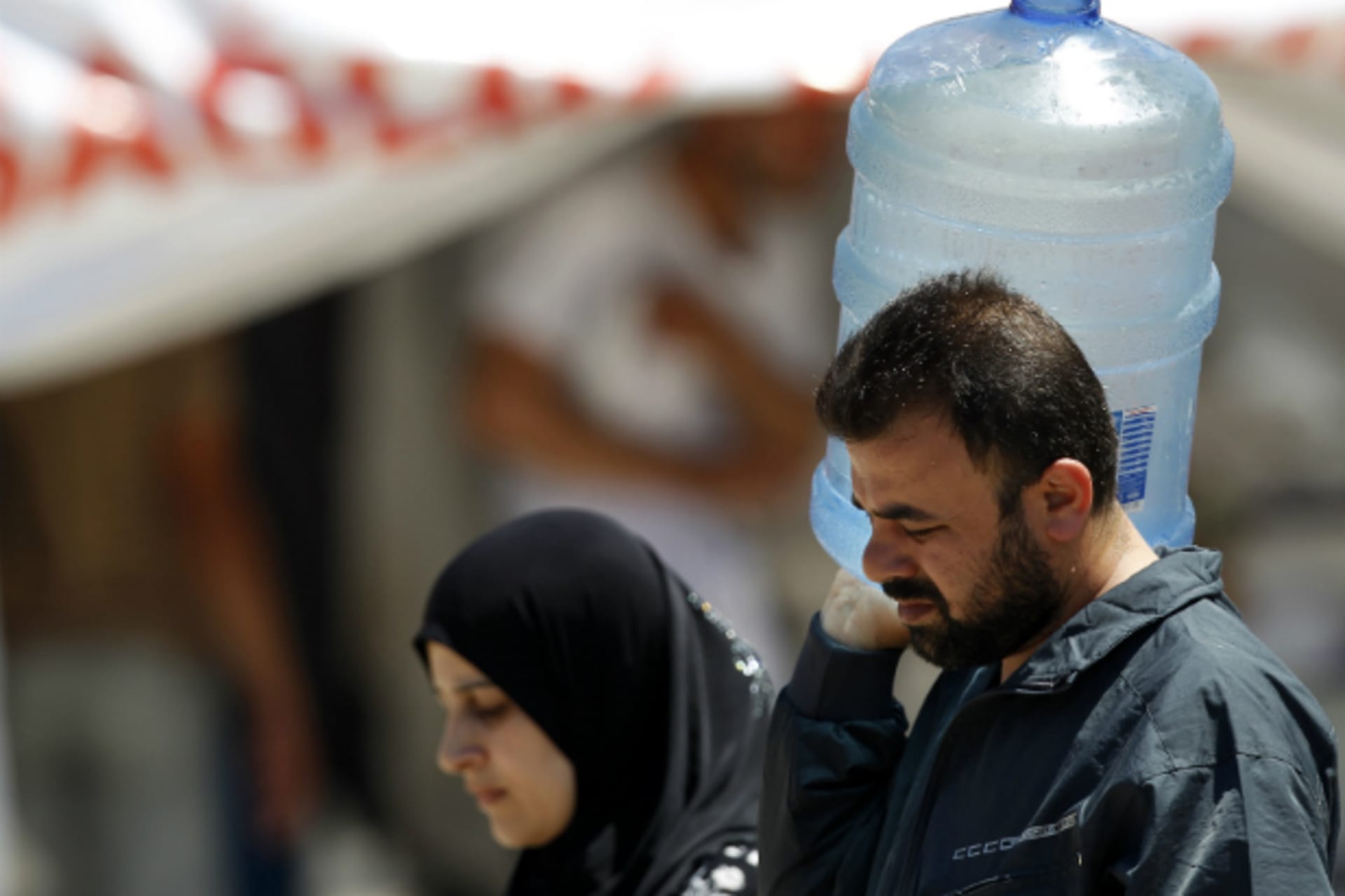 <p>A Syrian man carries a water container as he is accompanied by a woman at a refugee camp in the Turkish border town of Yayladagi (Reuters/Umit Bektas)</p>