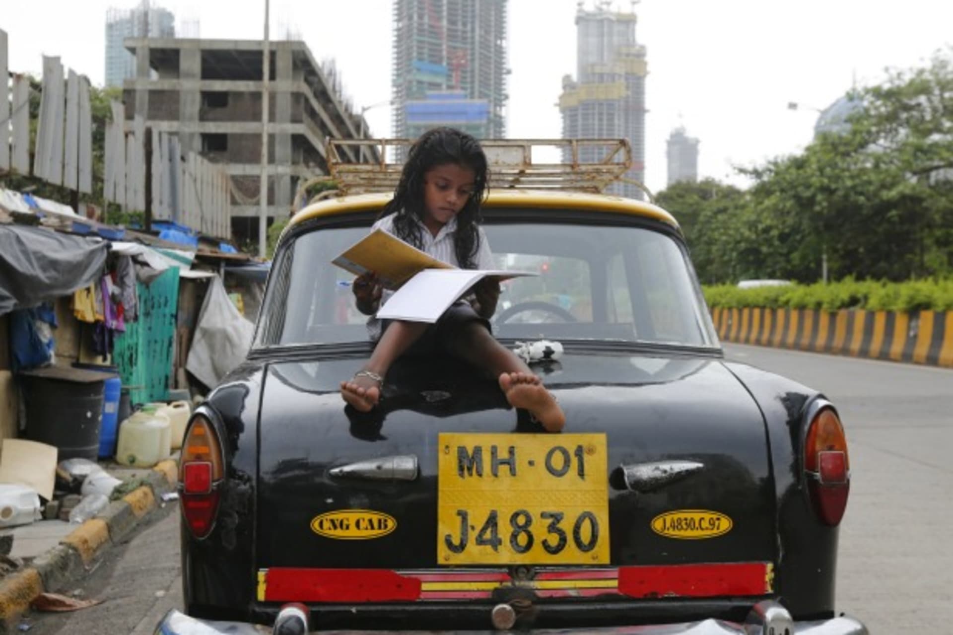 <p>A girl studies while sitting on top of a taxi outside her shanty home at a roadside in Mumbai, India (Shailesh Andrade/Reuters).</p>
