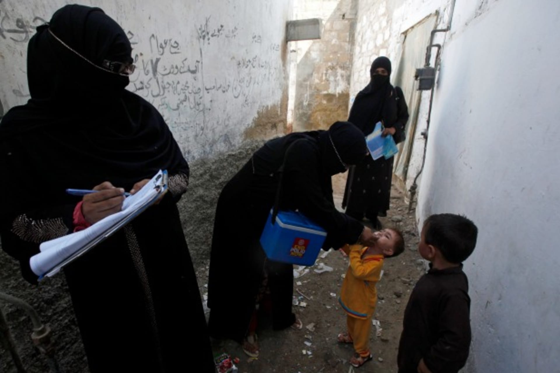 <p>A polio vaccinator administers polio vaccine drops to a boy while a colleague takes notes nearby in Karachi, Pakistan, October 2014 (Courtesy Reuters/Akhtar Soomro).</p>
