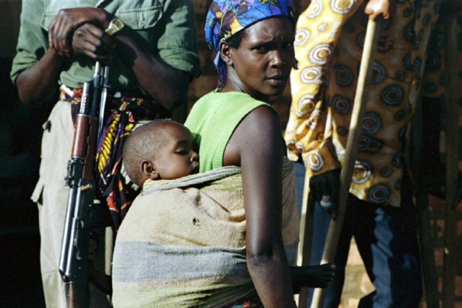 <p>A Tutsi woman passes between a guerilla from the Rwandan Patriotic Front on the left and a wounded man on the right, Rwanda, May 1994 (Courtesy Reuters).</p>
