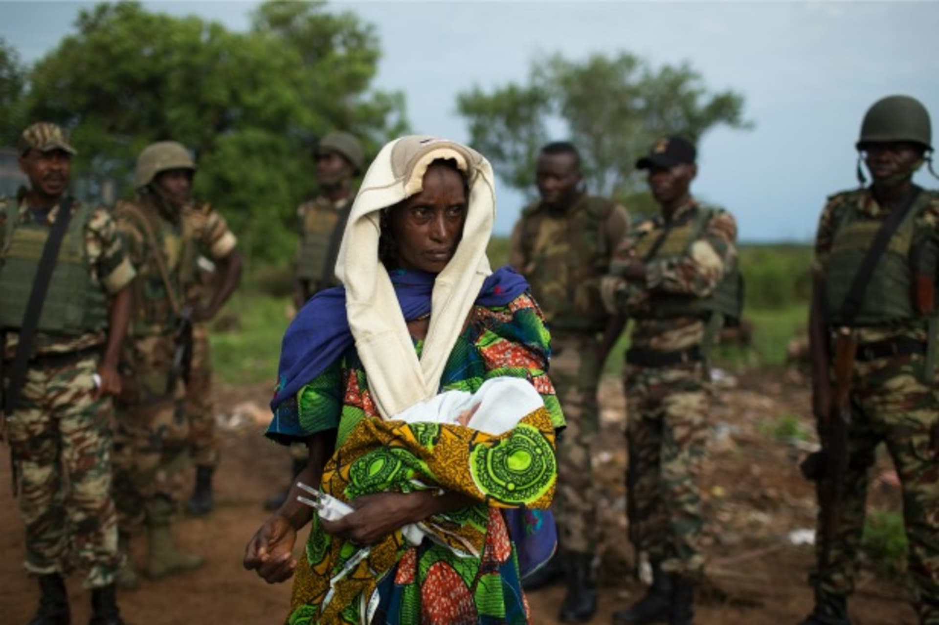 <p>A woman holding a newborn stands in front of African Union troops in the Central African Republic, April 2014 (Courtesy Reuters/Siegfried Modola).</p>

