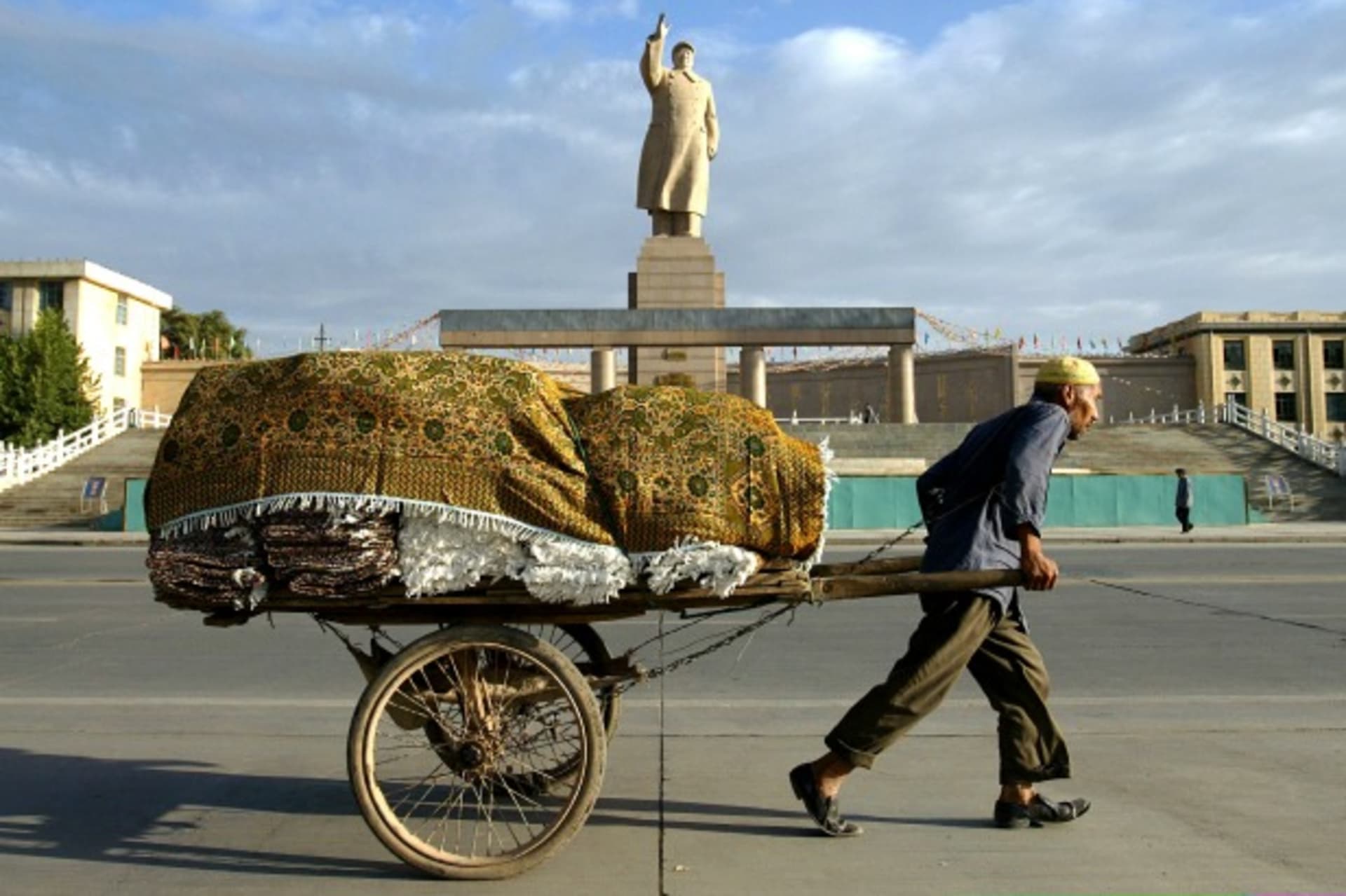 <p>A Uighur worker pulls a cart past a statue of the late chairman Mao Zedong at the People’s Square in Kashgar, China, September 2003 (Courtesy Reuters).</p>
