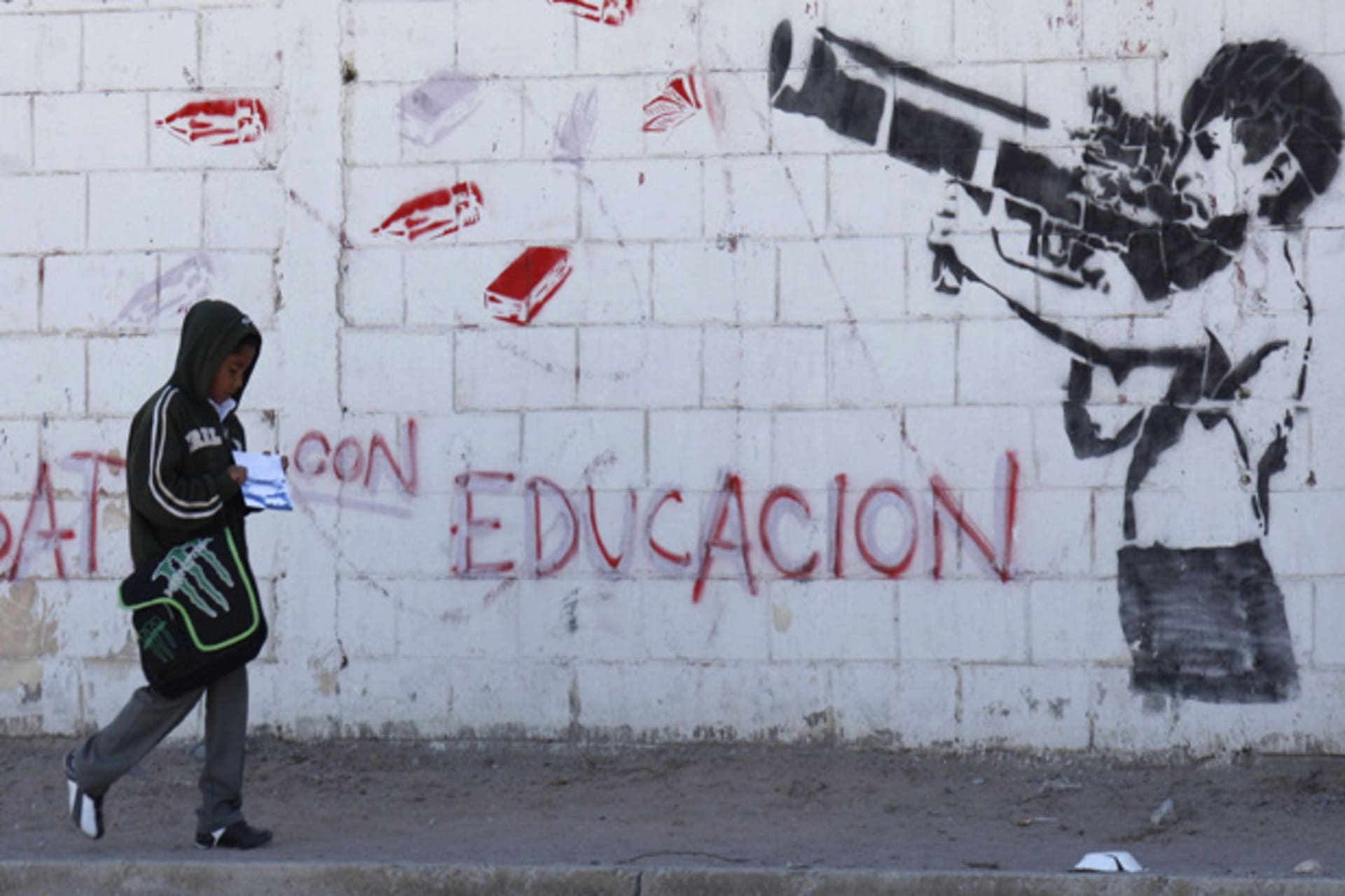 A boy walks past a mural depicting a child shooting an RPG loaded with school supplies in Ciudad Juarez