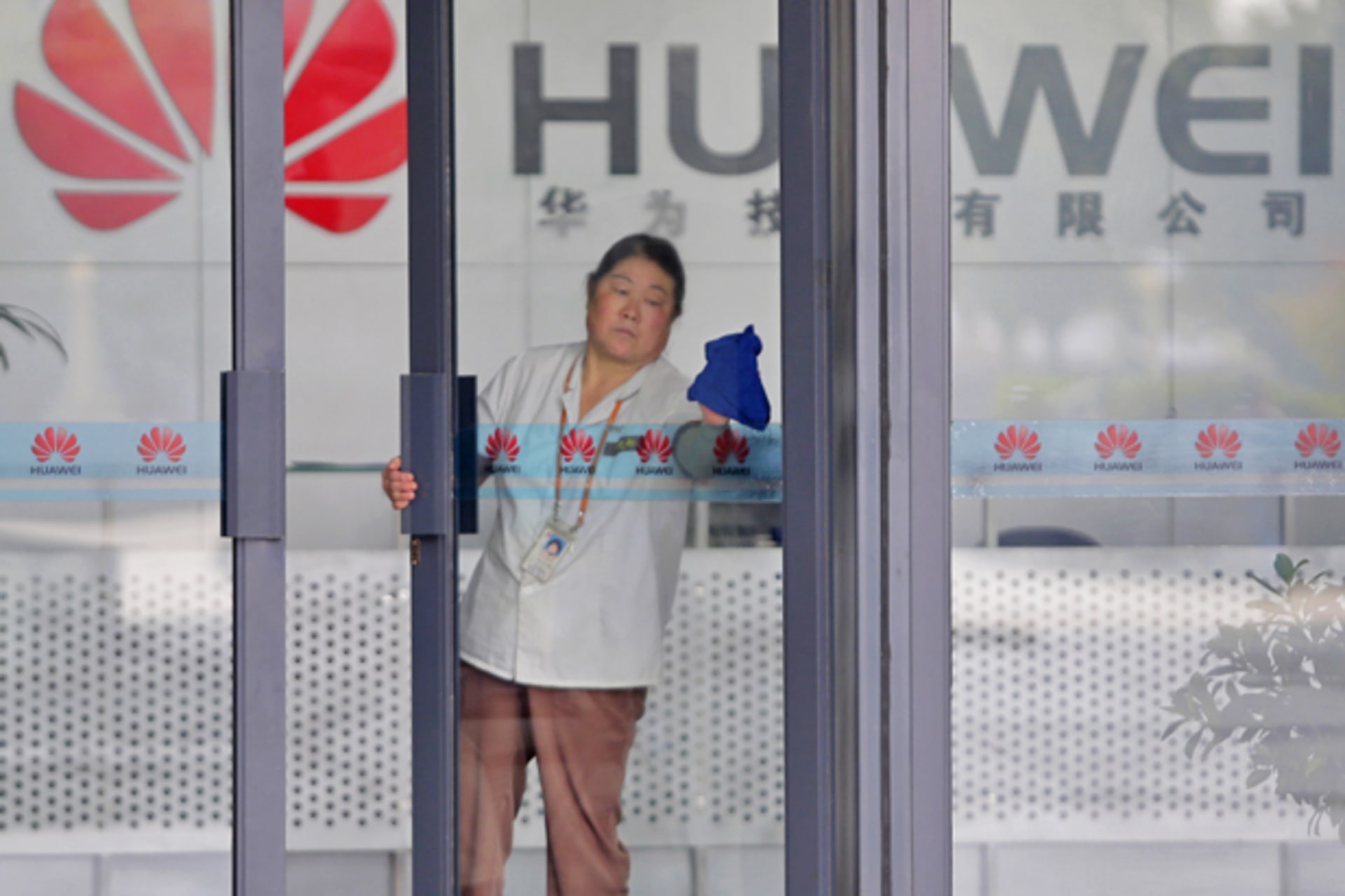 <p>A cleaner wipes the glass door of a Huawei office in Wuhan, Hubei province (Courtesy Reuters).</p>
