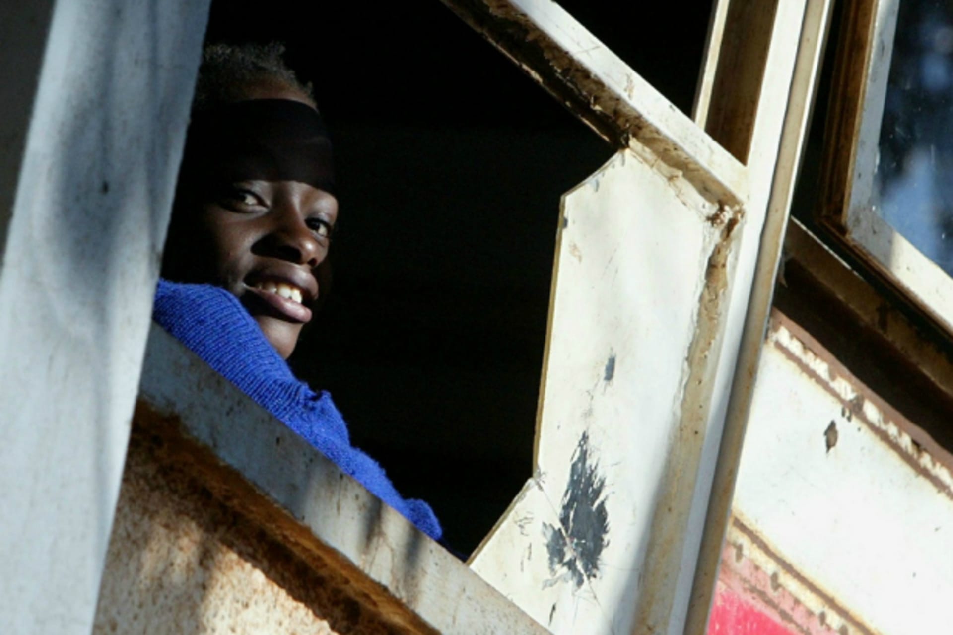 <p>A Kenyan student looks through a broken window in a classroom in Nairobi, Kenya, January 2005 (Courtesy Reuters/Antony Njuguna).</p>
