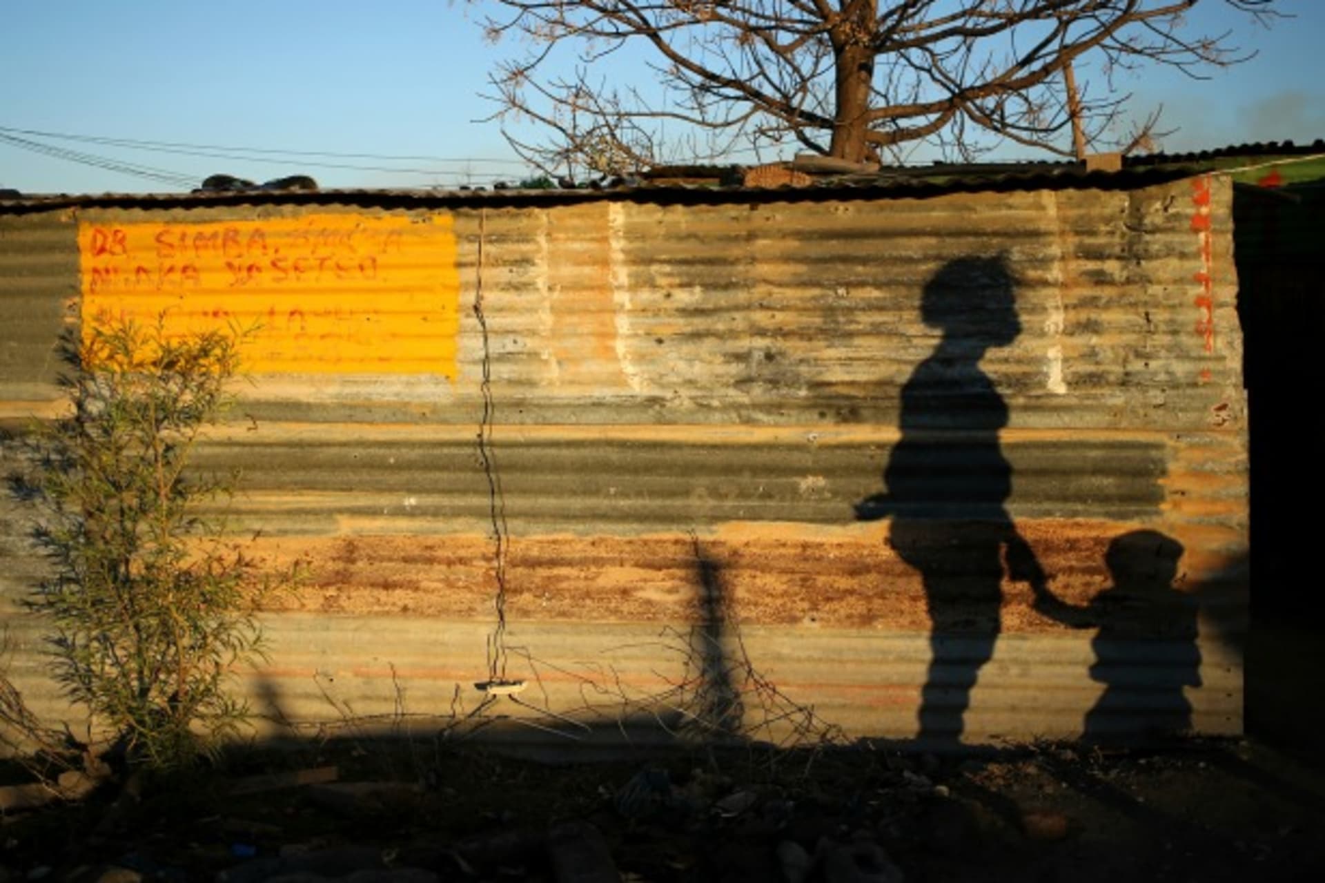 <p>The shadows of a mother and child are cast on a shack in Marikana’s Nkaneng township in Rustenburg,South Africa, August 2013 (Courtesy Reuters/Siphiwe Sibeko).</p>
