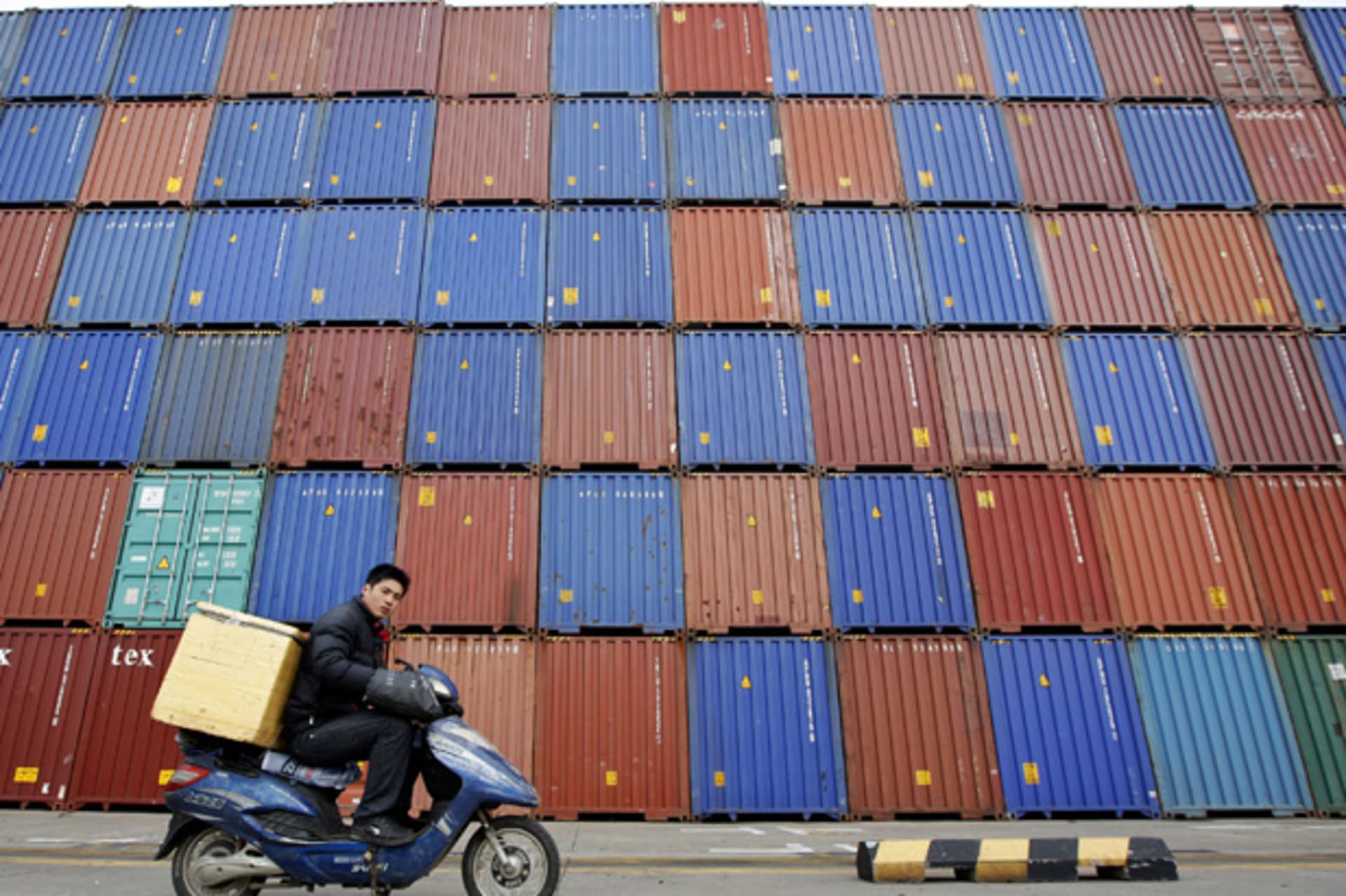 <p>A man rides his motorcycle past shipping containers at the Port of Shanghai (Aly Song/Courtesy Reuters).</p>
