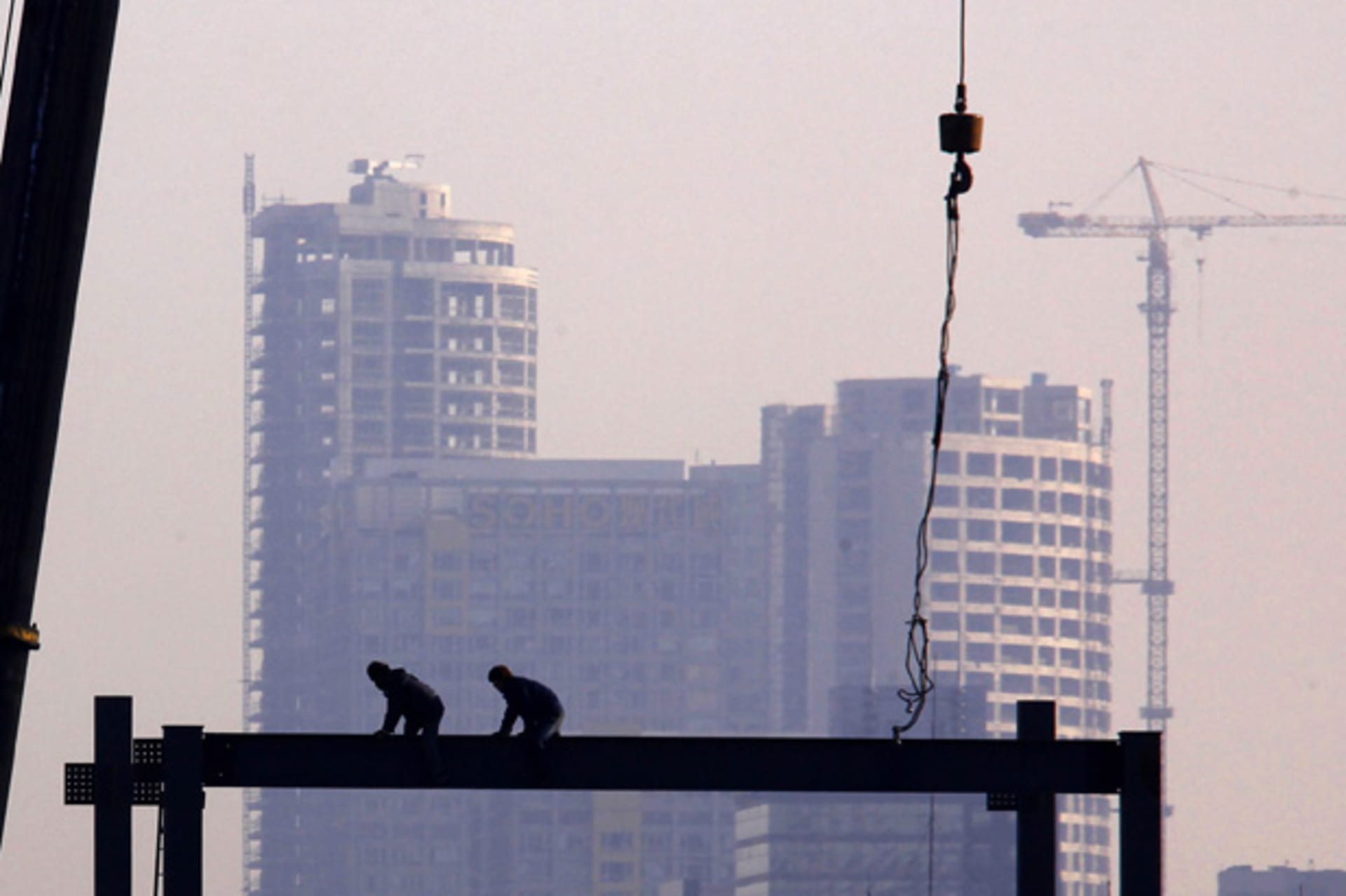 <p>Workers crawl along a steel pylon on top of a building under construction in central Beijing (David Gray/Courtesy Reuters).</p>
