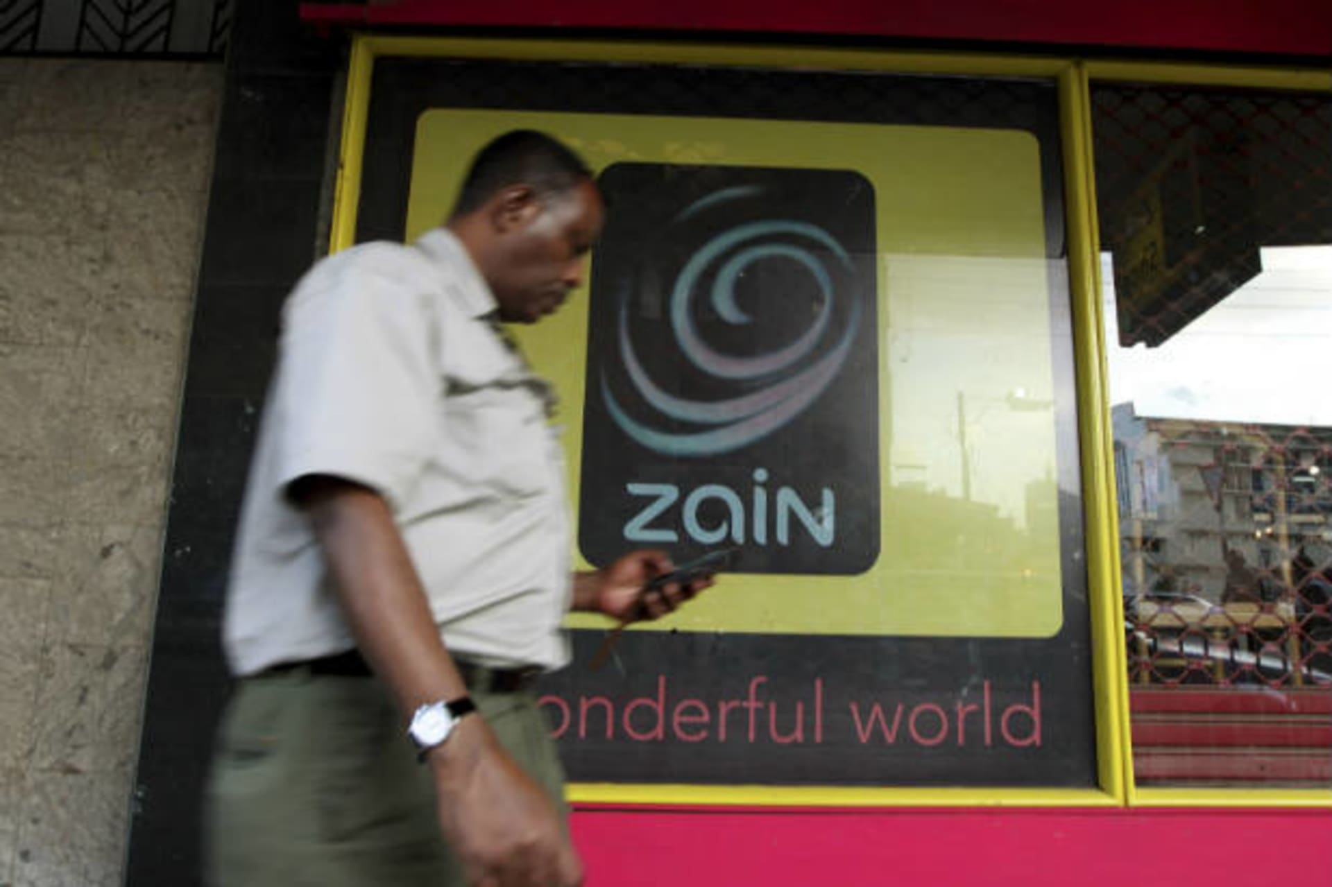 <p>A man uses his mobile phone as he walks past a Zain customer care shop in Nairobi on February 15, 2010 (Thomas Mukoya/Courtesy Reuters).</p>
