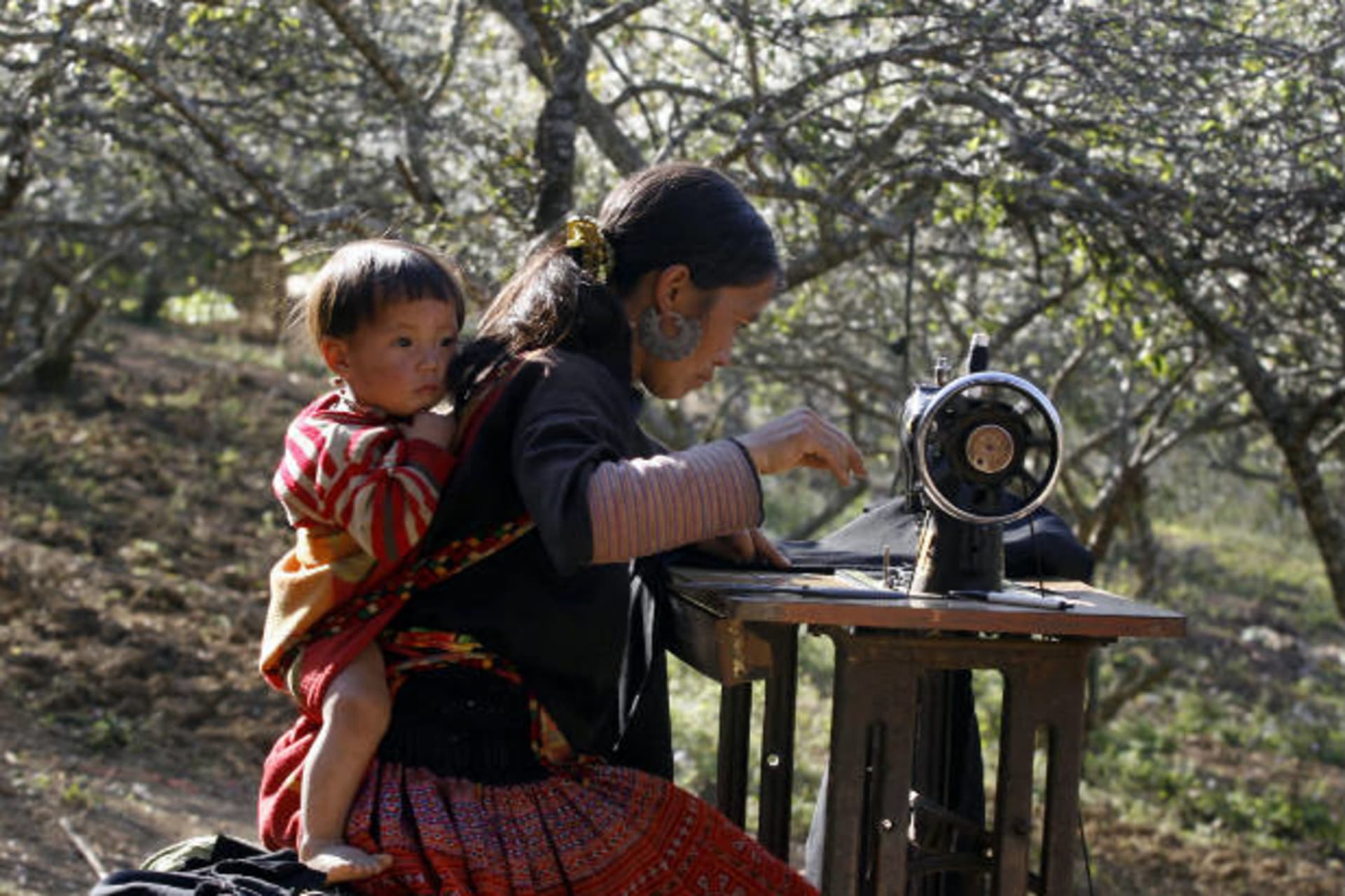 <p>A Hmong woman holds her son on her back while sewing in a northern province of Vietnam on January 1, 2010 (Nguyen Huy Kham/Courtesy Reuters).</p>
