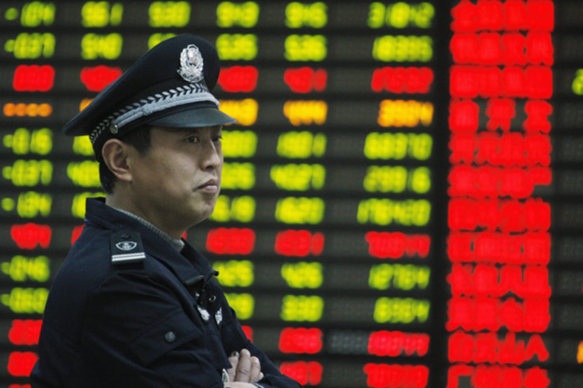 A security guard stands in front of an electrical board displaying stock information at a brokerage house in Huaibei