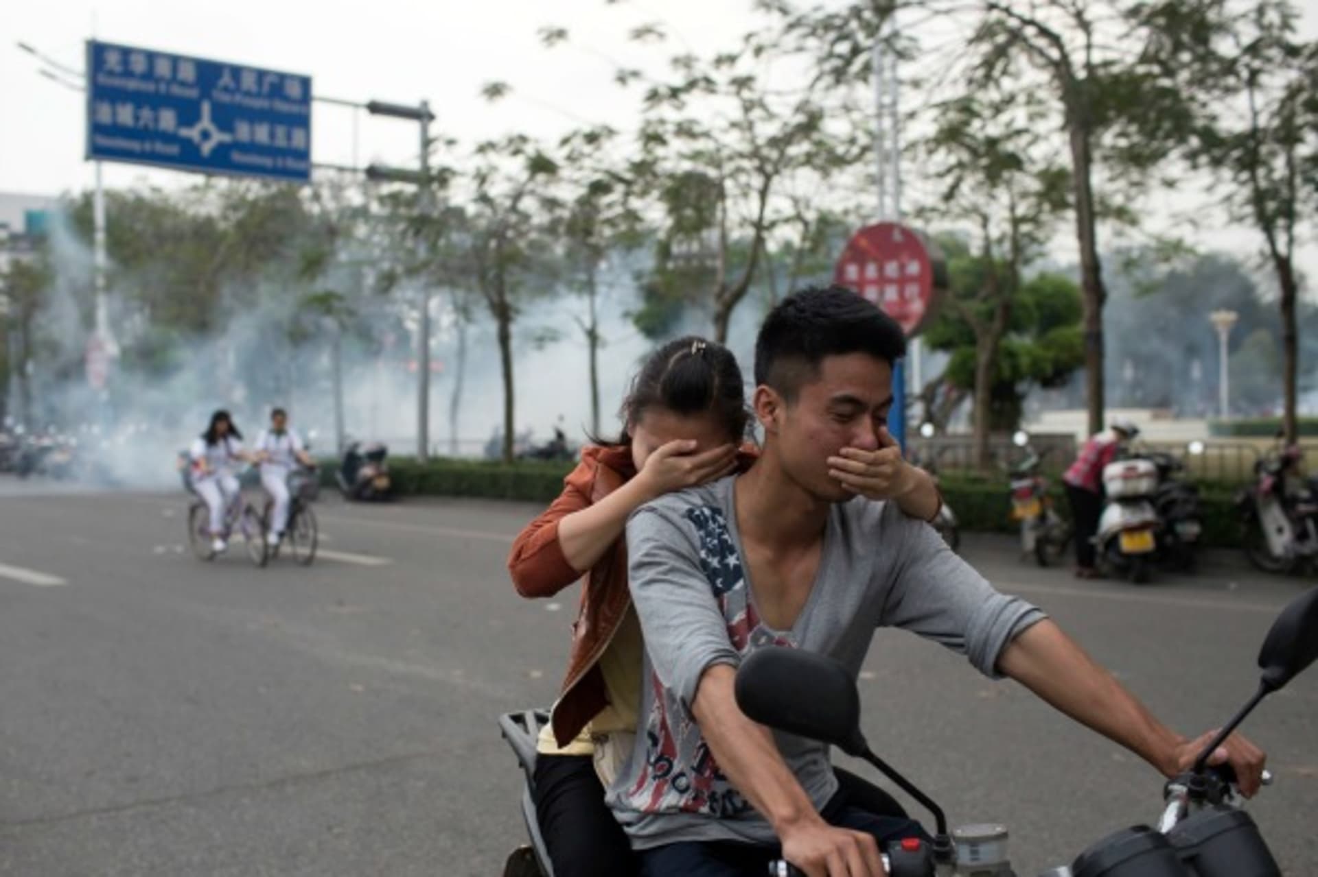 <p>Residents cover their faces as they ride a motorcycle along a street after tear gas was released by police to disperse a protest against a chemical plant project in Maoming, Guandong province, China on March 31, 2014. (Stringer/Courtesy Reuters)</p>
