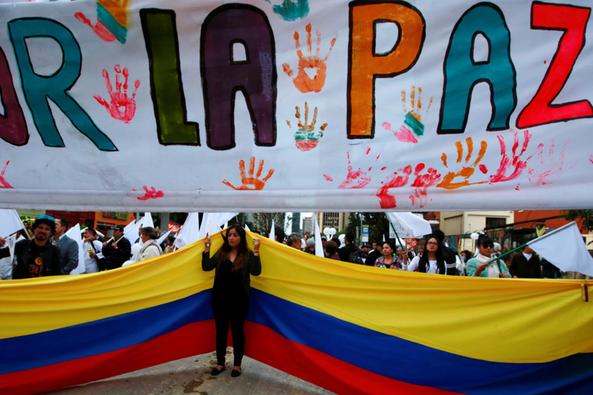 <p>A supporter rallying for a peace agreement between the Colombian government and FARC stands under a banner reading “for peace” during a march in Bogota.</p>