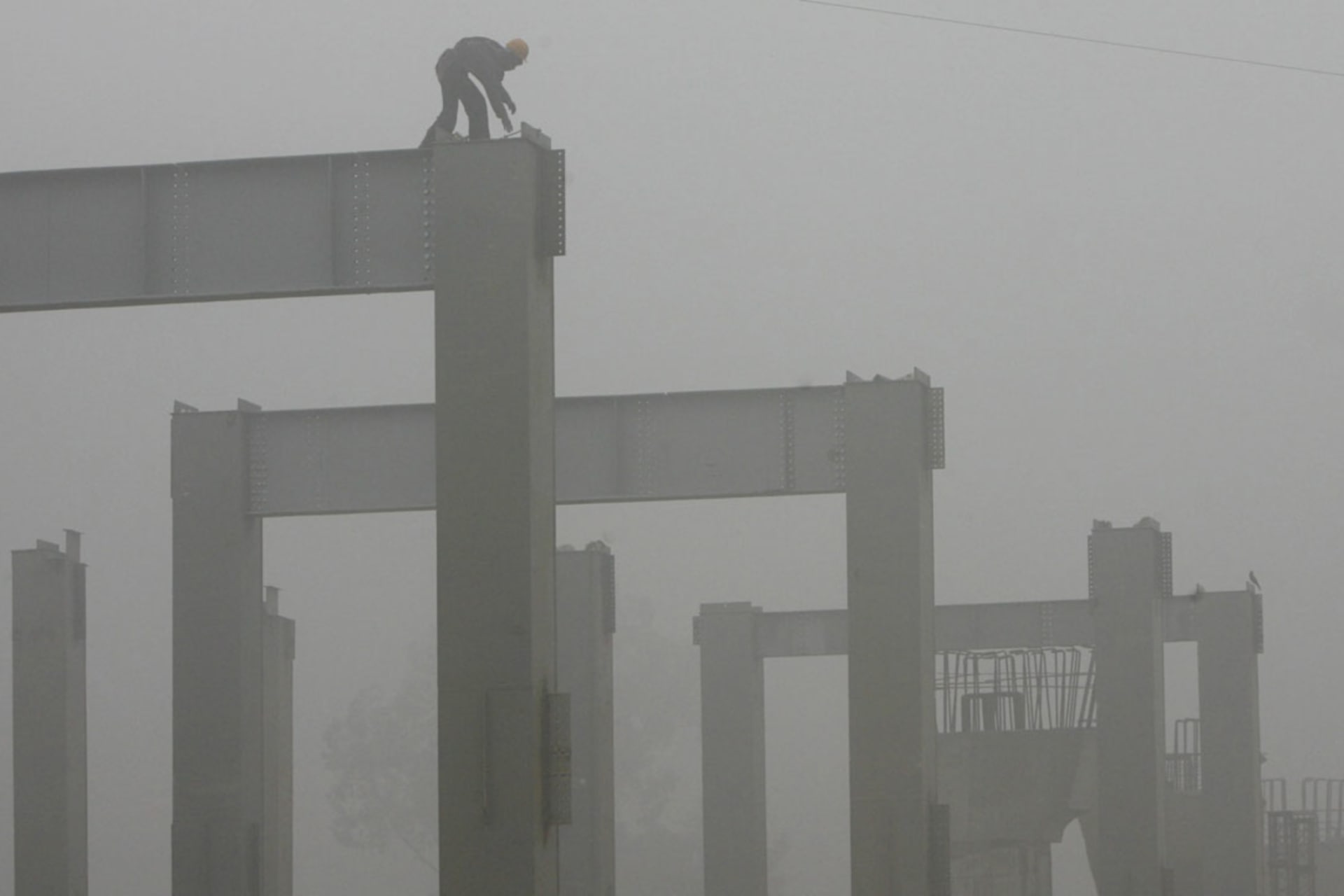 <p>A Delhi Metro Rail Corporation worker works amidst thick fog at a construction site in New Delhi.</p>
