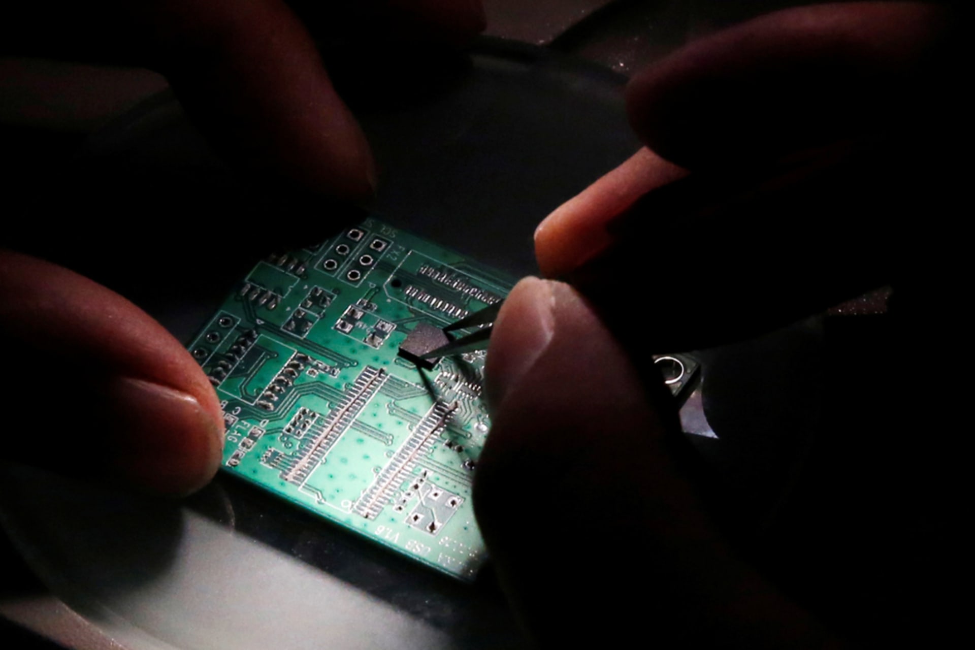<p>A researcher plants a semiconductor on an interface board, which is placed under a microscope. </p>
