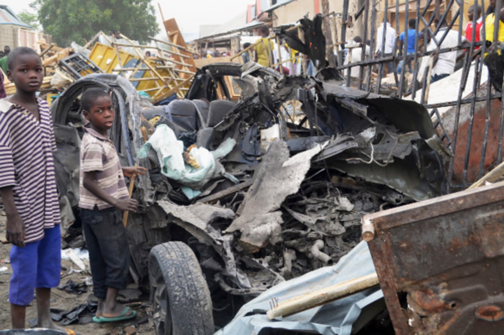 Two boys stand near the charred chassis of a vehicle after a bomb attack near a busy market area in Ajilari-Gomari near the city's airport, in Maiduguri March 2, 2014.