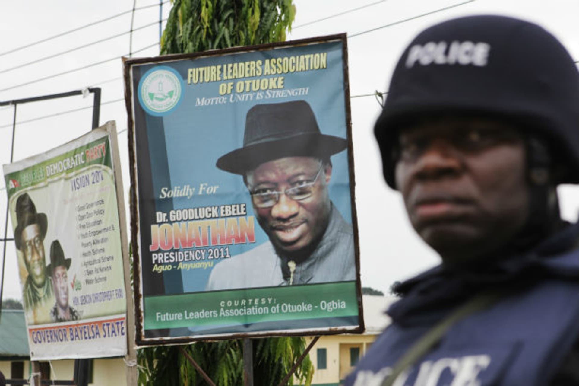 An armed police officer in riot gear stands guard in front of a poster of Nigerian incumbent President Goodluck Jonathan in Otuoke 16/04/2011.
