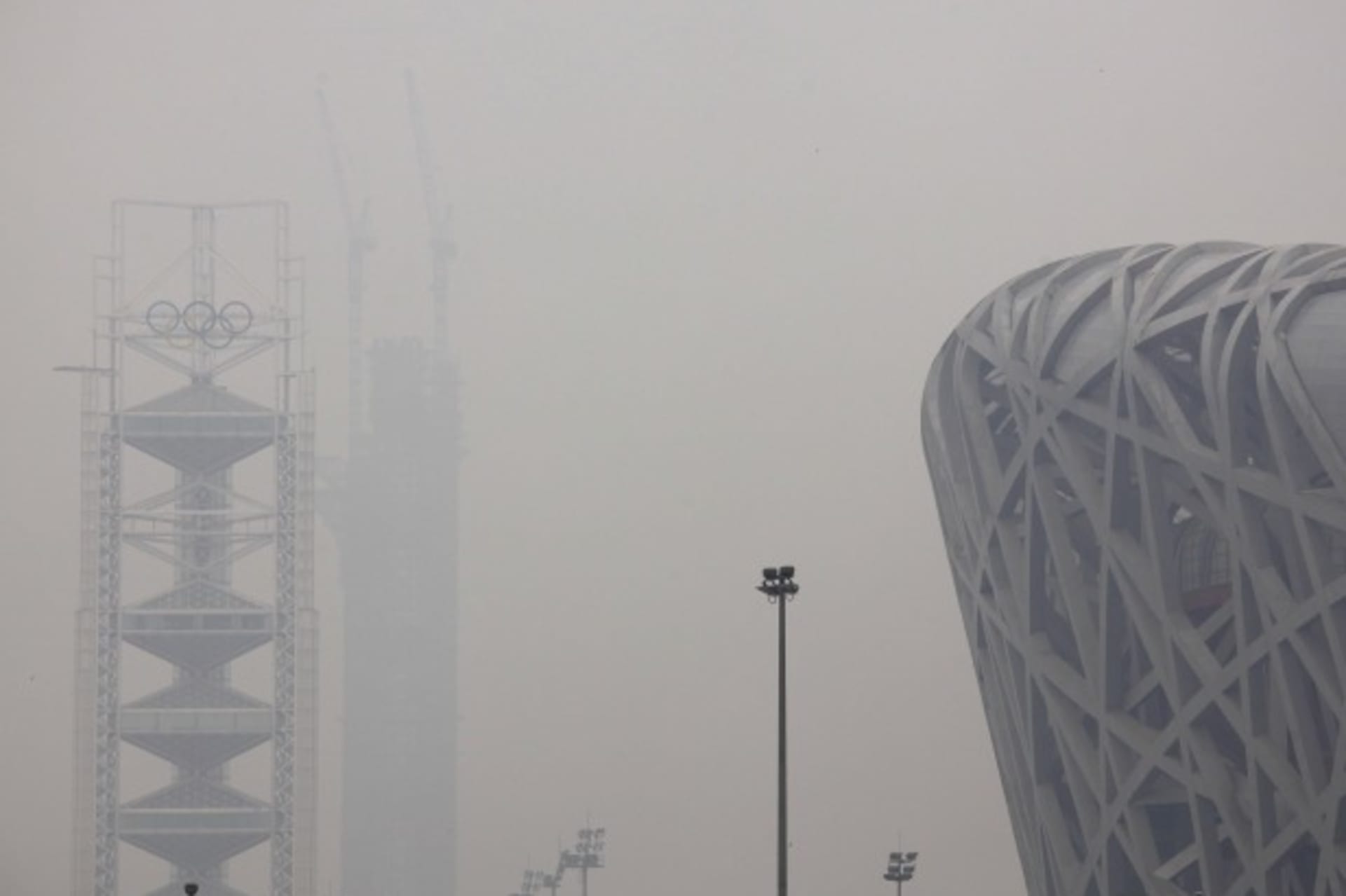 <p>The National Stadium, also known as the ‘Bird’s Nest’, can be seen next to a tower bearing the Olympic rings and a building under construction on a high air pollution day in Beijing on June 6, 2012.</p>
