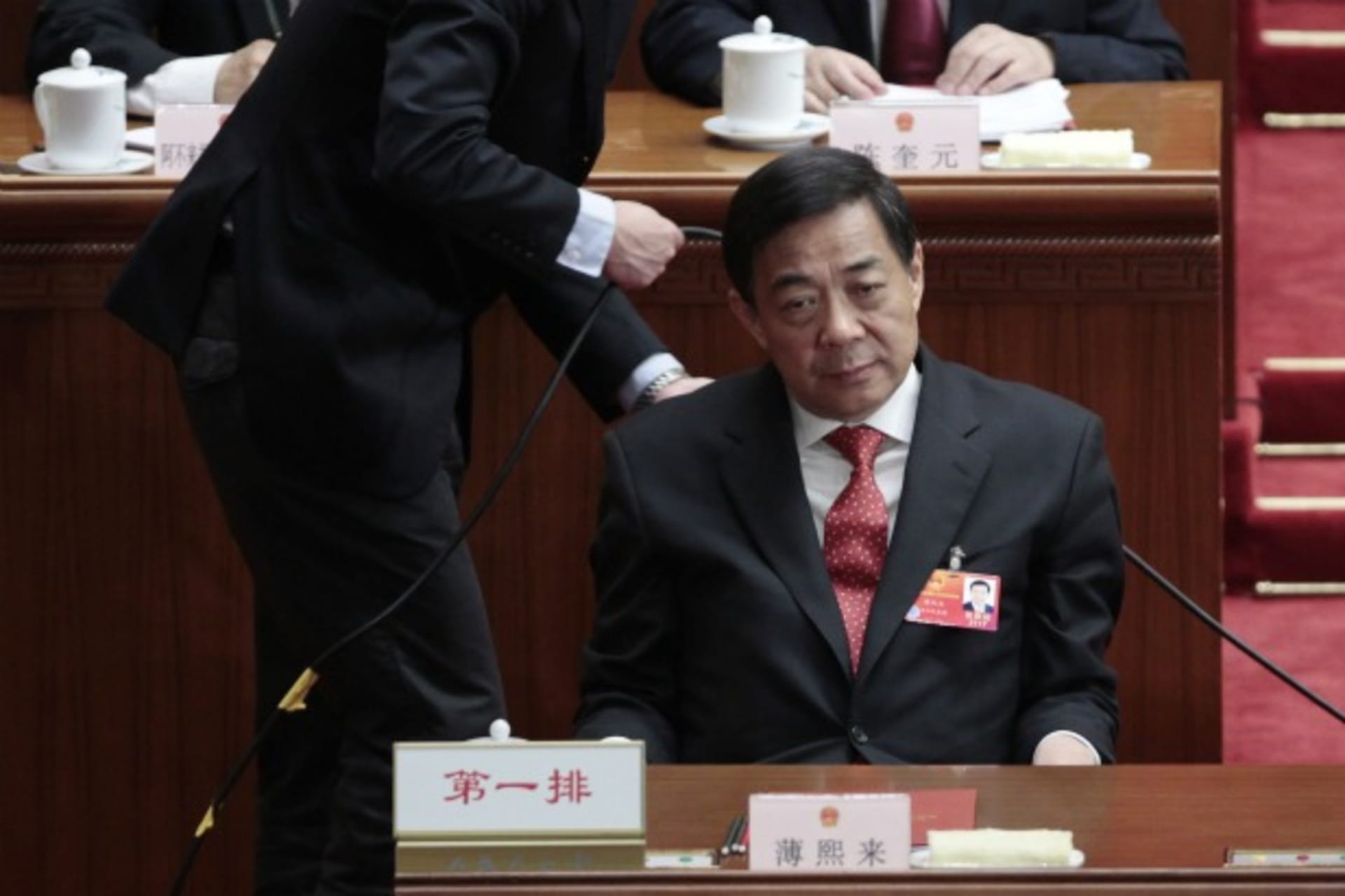 <p>Bo Xilai pauses as a man adjusts a cable behind him during the closing ceremony of the National People’s Congress at the Great Hall of the People in Beijing on March 14, 2012. (Jason Lee / Courtesy of Reuters)</p>

