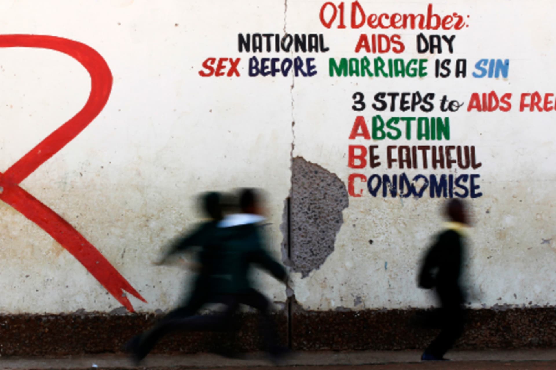 Children run past a mural painting of an Aids ribbon at a school in Khutsong Township, 74 km (46 miles) west of Johannesburg, August 22, 2011