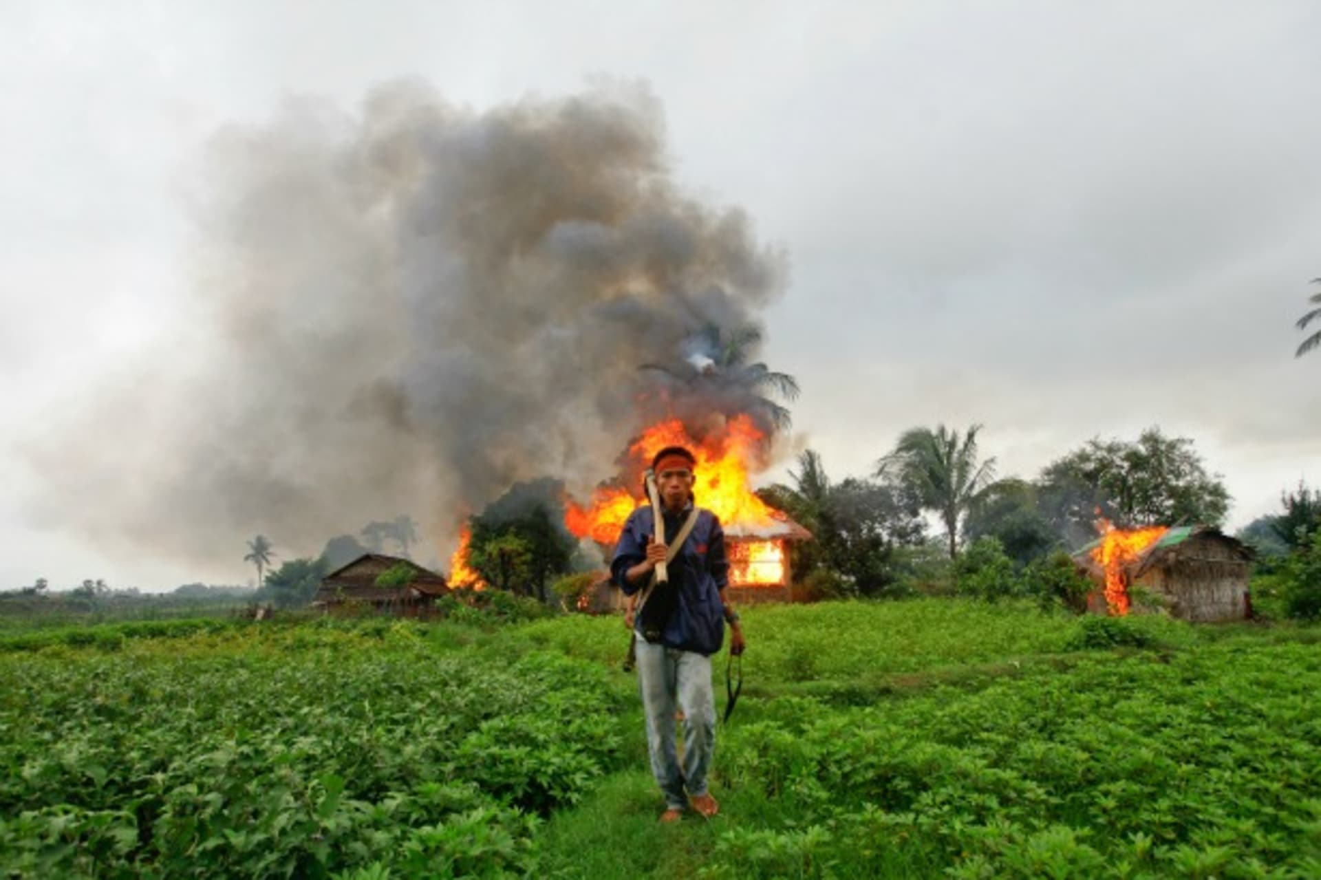 <p>An ethnic Rakhine man holds homemade weapons as he walks in front of houses that were burnt during fighting between Buddhist Rakhine and Muslim Rohingya communities in Sittwe on June 10, 2012.</p>
