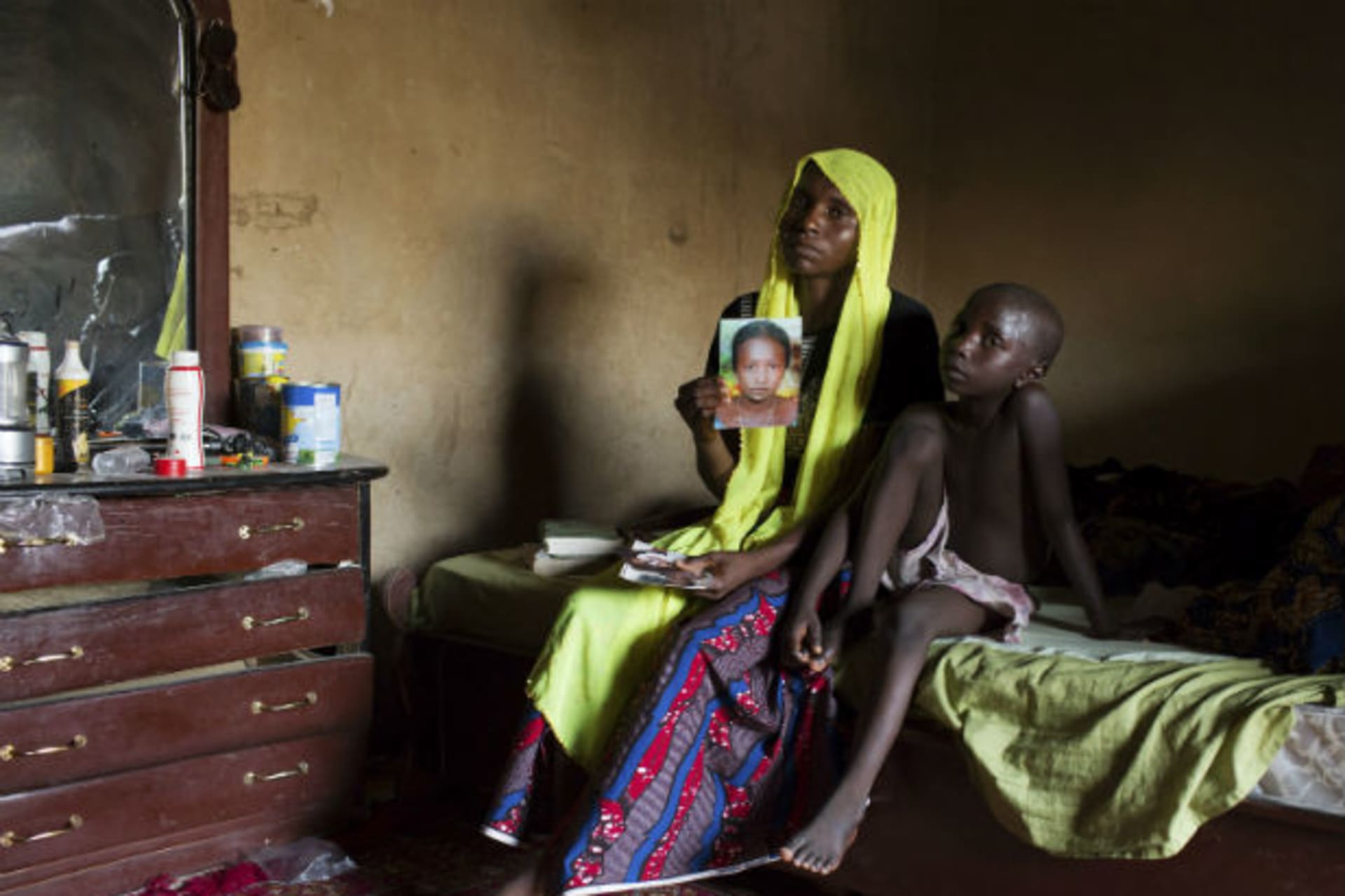 Rachel Daniel, 35, holds up a picture of her abducted daughter Rose Daniel, 17, as her son Bukar, 7, sits beside her at her home in Maiduguri, May 21, 2014. (Joe Penney/Courtesy Reuters)