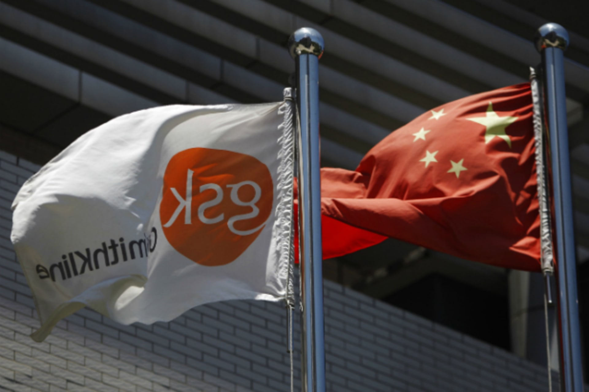 <p>A flag (L) bearing the logo of GlaxoSmithKline (GSK) flutters next to a Chinese national flag outside a GlaxoSmithKline office building in Shanghai on July 12, 2013.</p>