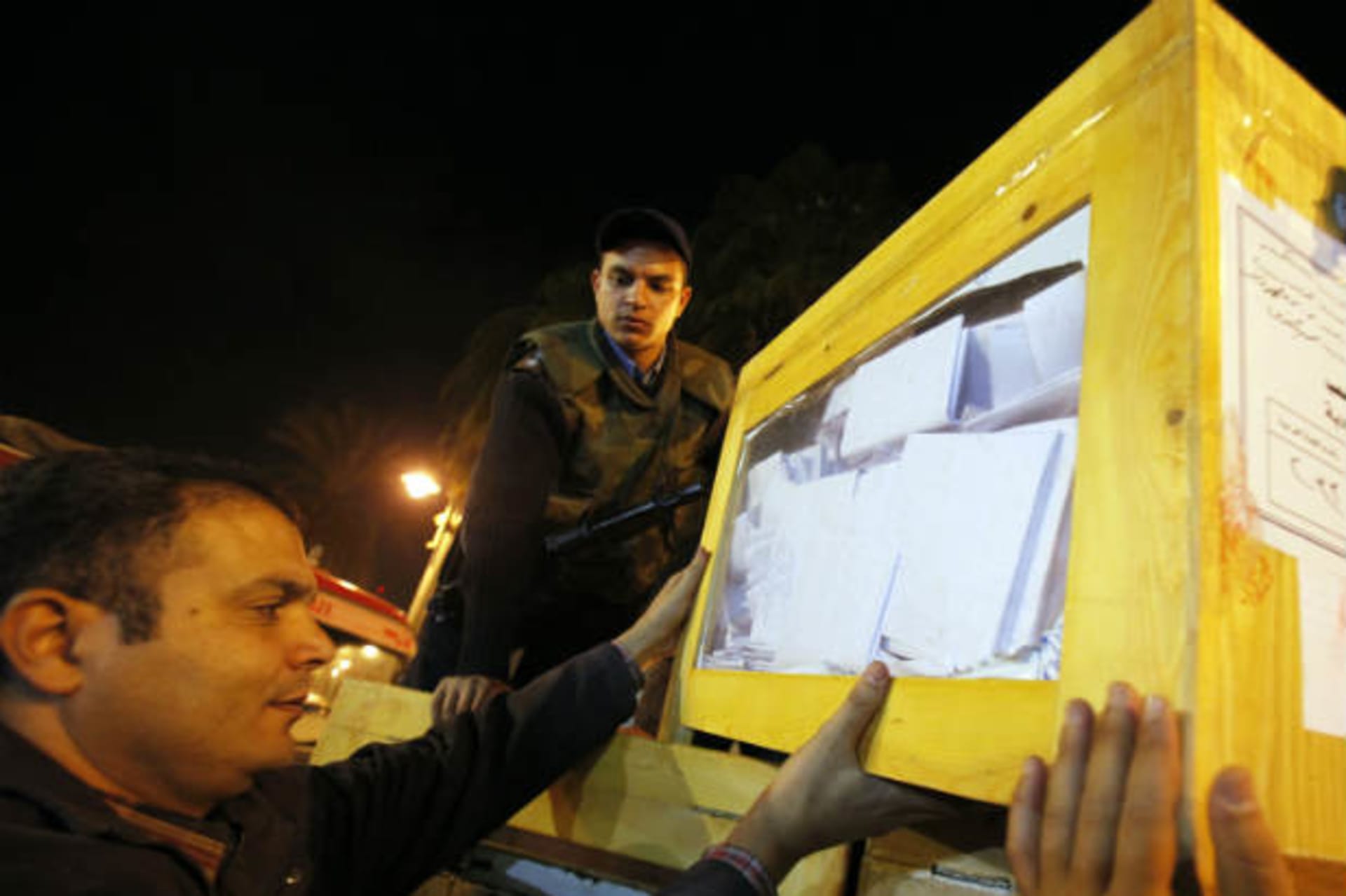 Egyptian electoral workers carry ballot box at a center for vote counting during a previous parliamentary election (El-Ghany/Courtesy Reuters).