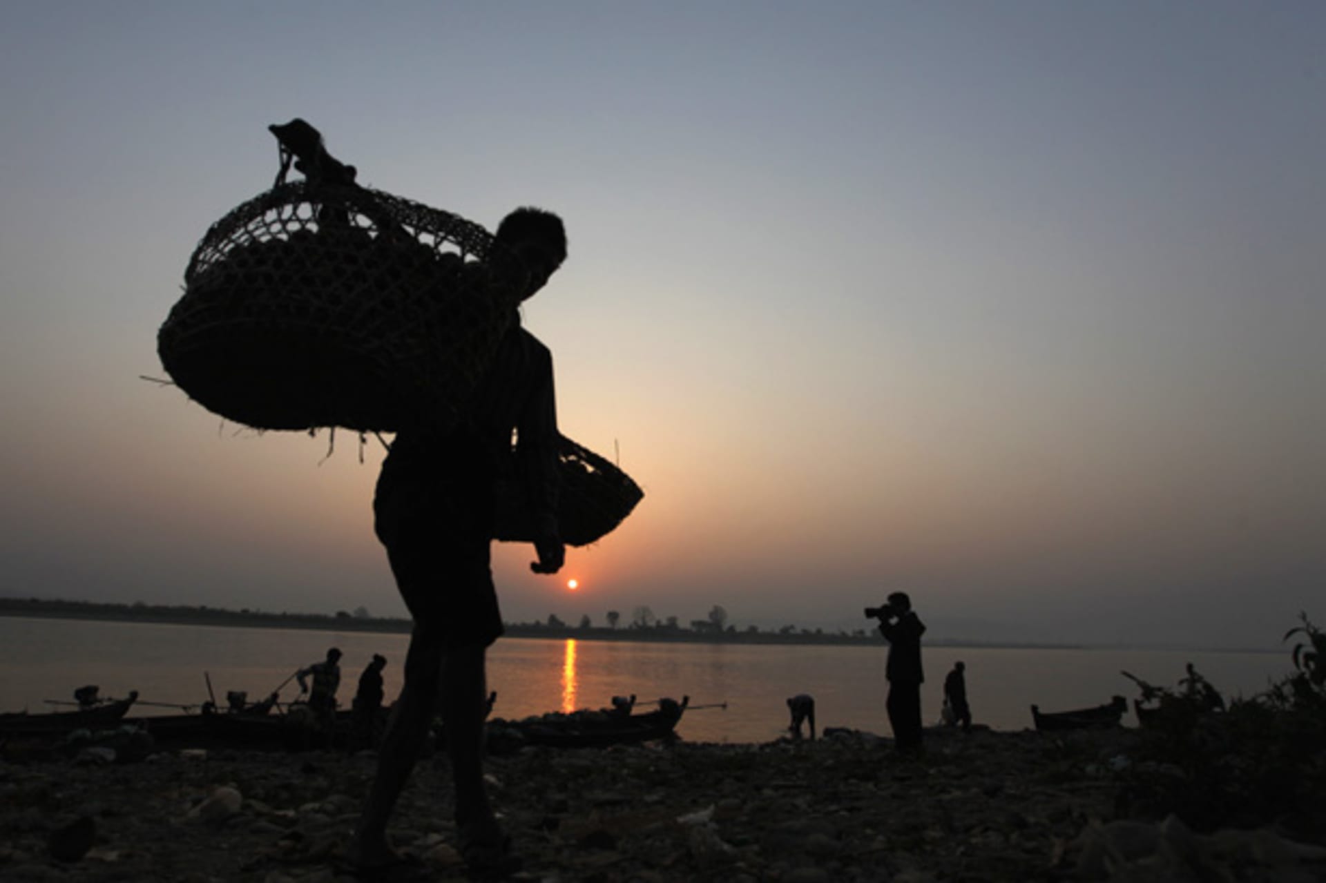 <p>A Burmese man unloads tomatoes from a small boat along the Irrawaddy river banks. Some analysts worry about the consequences of a gluttony of foreign investment in Myanmar.</p>
