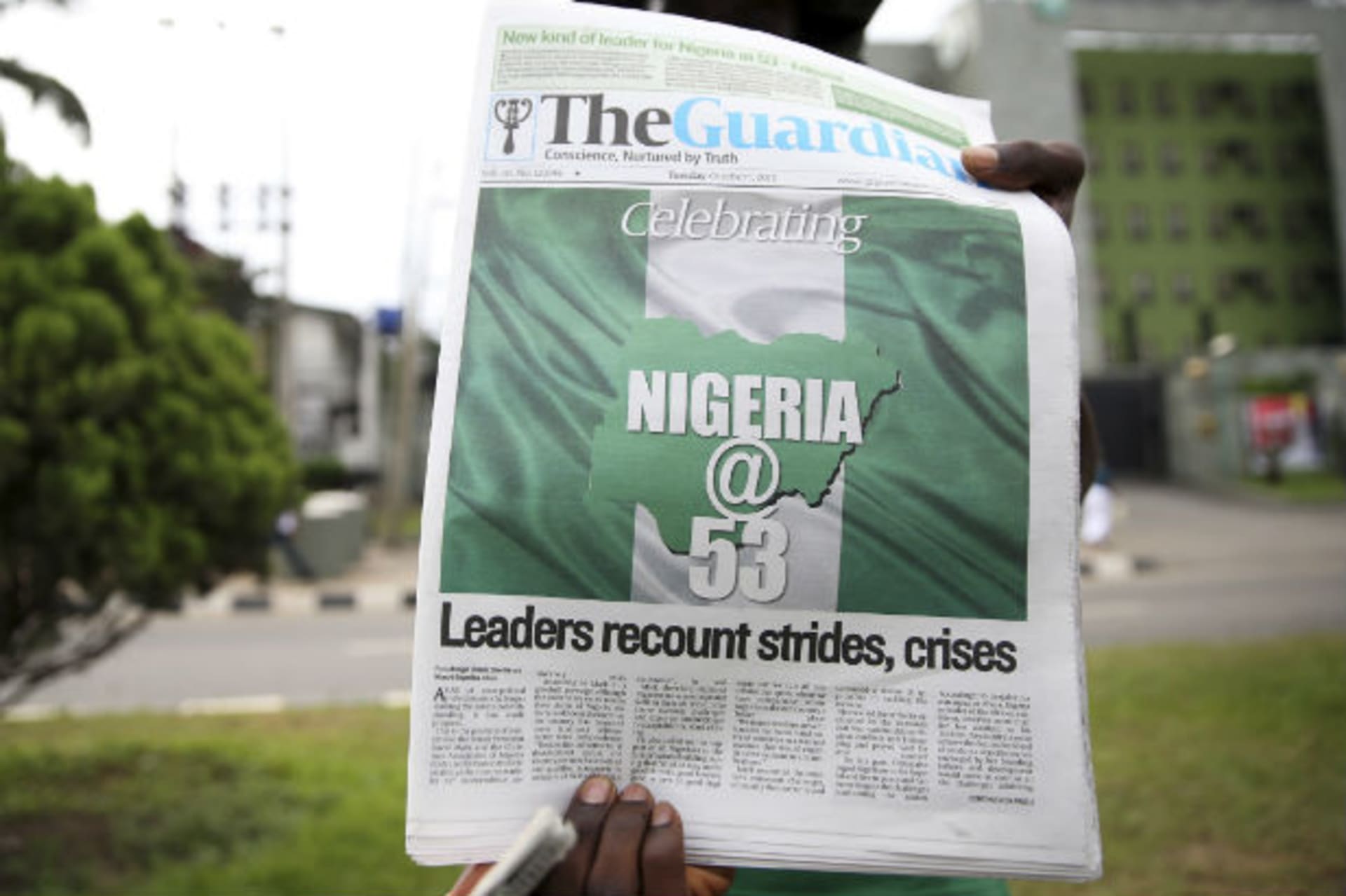 A vendor holds up a newspaper with a front page showing the colours of Nigeria on its 53rd independence celebration, along a road in Ikeja district in Lagos October 1, 2013.