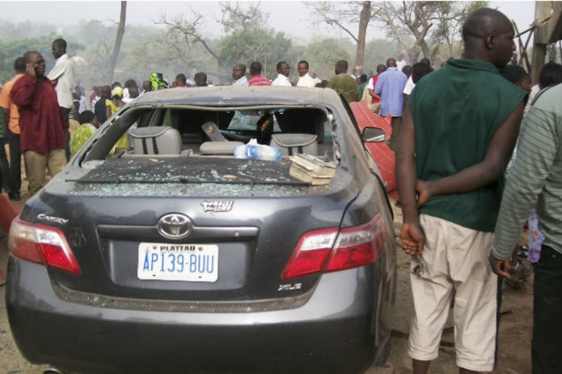 People stand by a damaged vehicle at a church, the site of a bomb blast, in Nigeria's central city of Jos February 26, 2012.