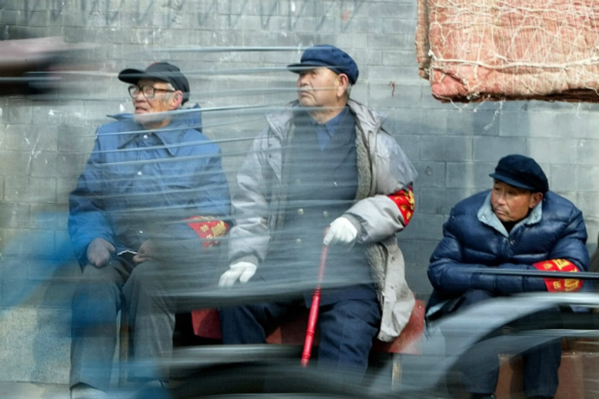 <p>Chinese cyclists ride past three elderly men from neighborhood watch committees in central Beijing on February 27, 2003.</p>
