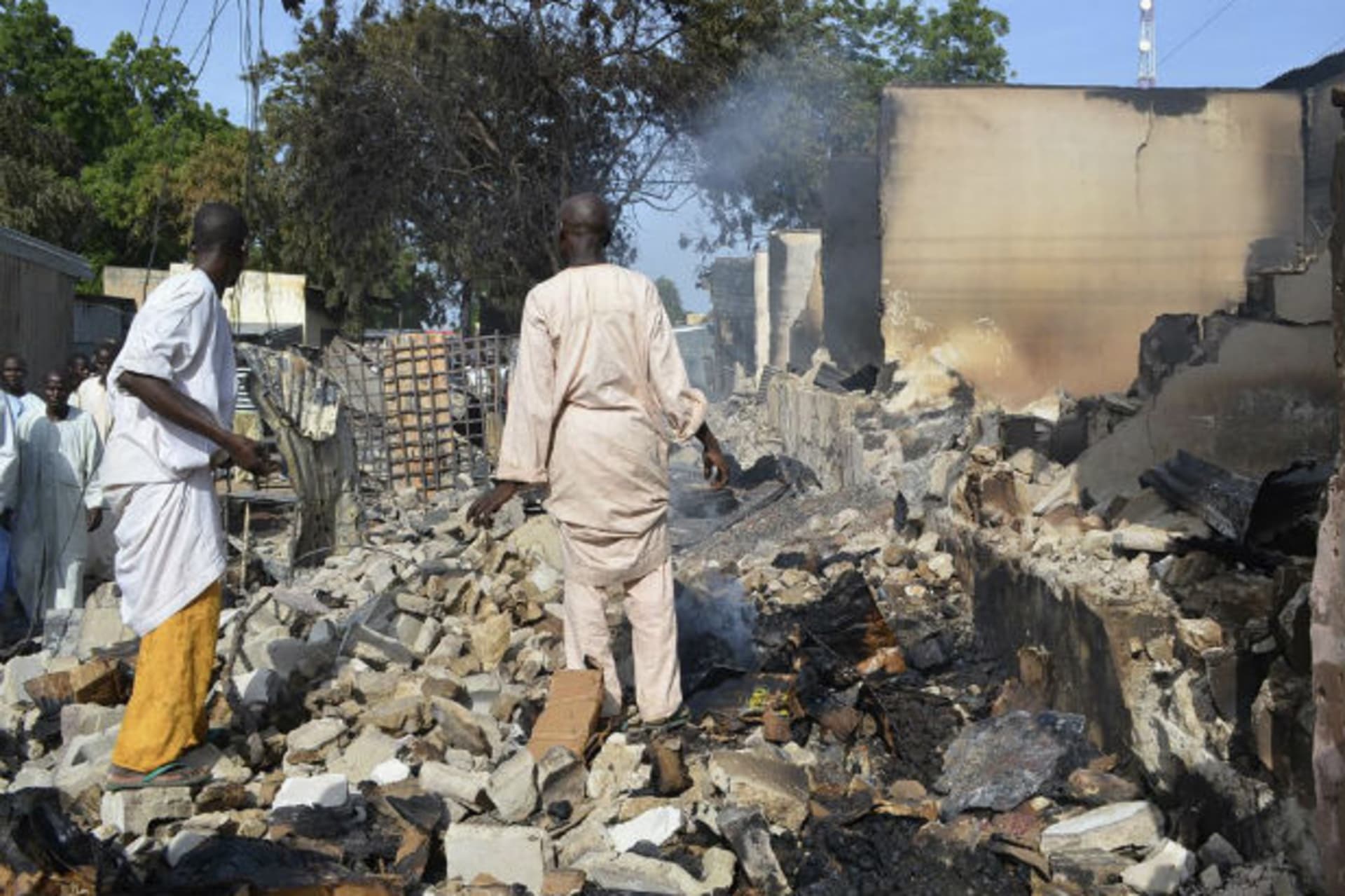 Residents watch as two men walk amidst rubble after Boko Haram militants raided the town of Benisheik, west of Borno State capital Maiduguri September 19, 2013.