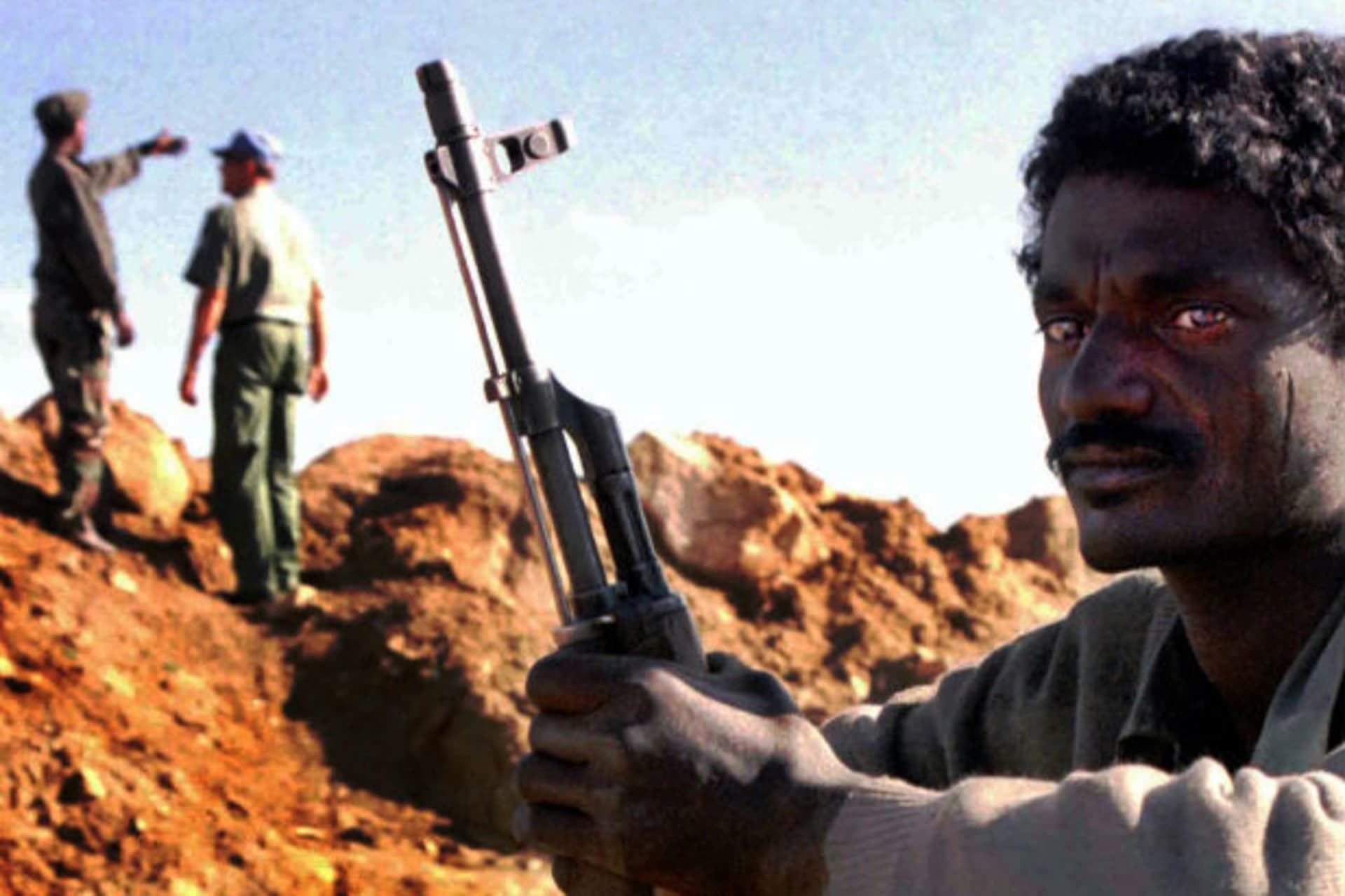 An Eritrean soldier sits on guard duty as a UN military observer and his Eritrean counterpart inspect a frontline trench near the Eritrean town of Senafe on October 20, 2000.