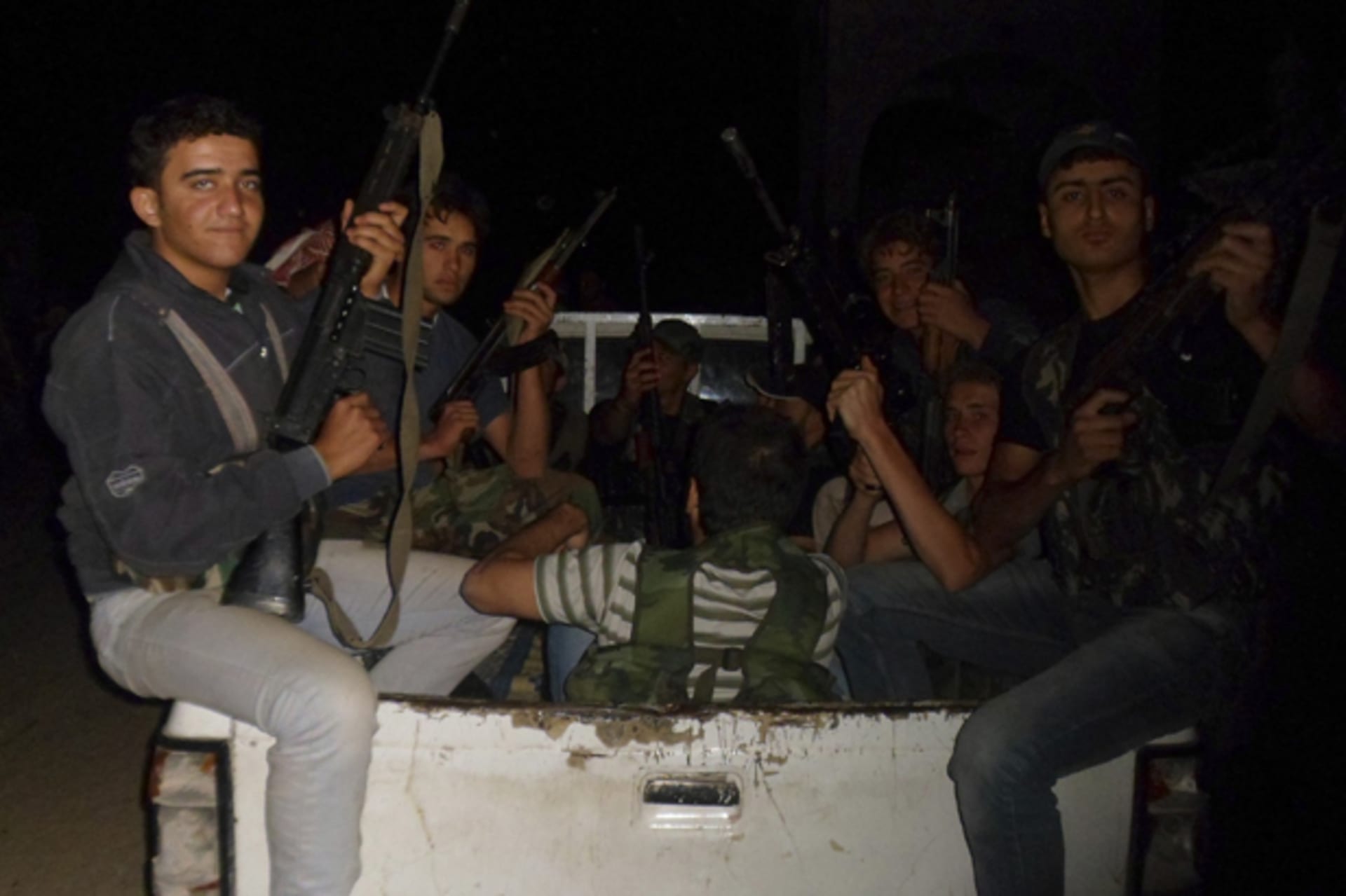 Members of the Free Syrian Army holding weapons sit at the back of a truck in Aleppo