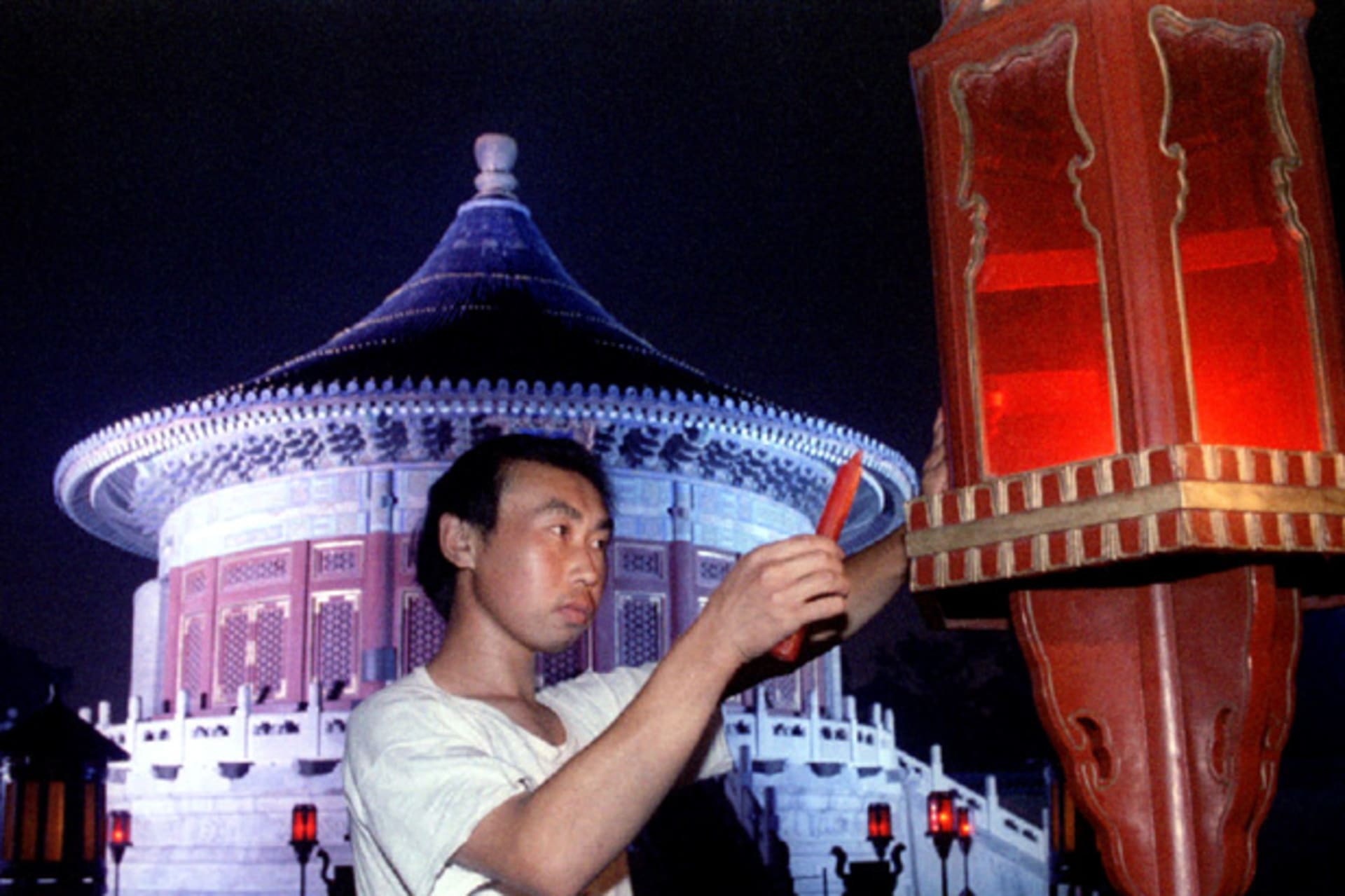 A worker replaces a candle in a lantern in front of The Imperial Vault of Heaven at the Temple of He..
