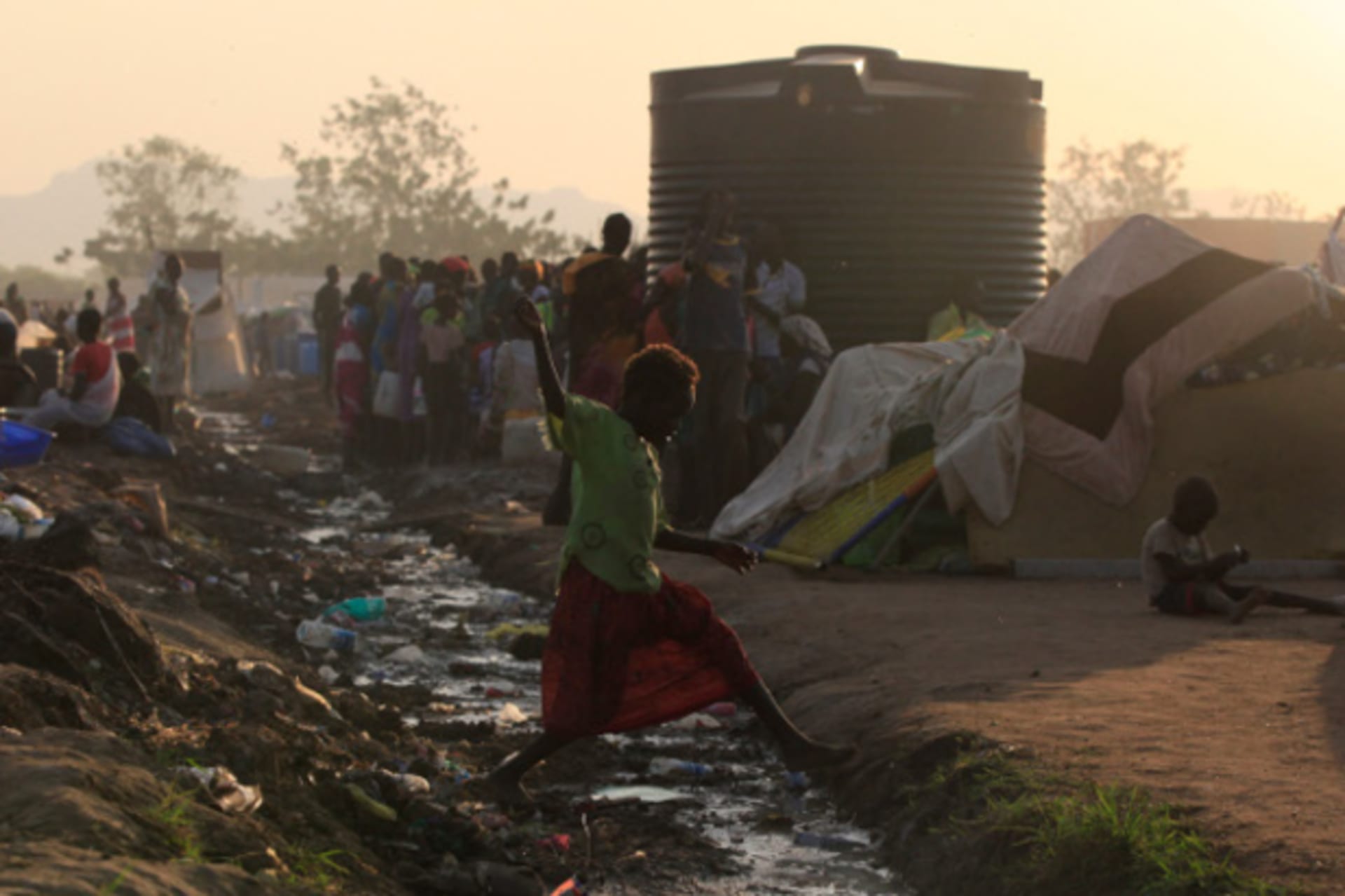 A barefoot girl jumps over an open drain filled with rubbish at Tomping camp in Juba, January 10, 2014