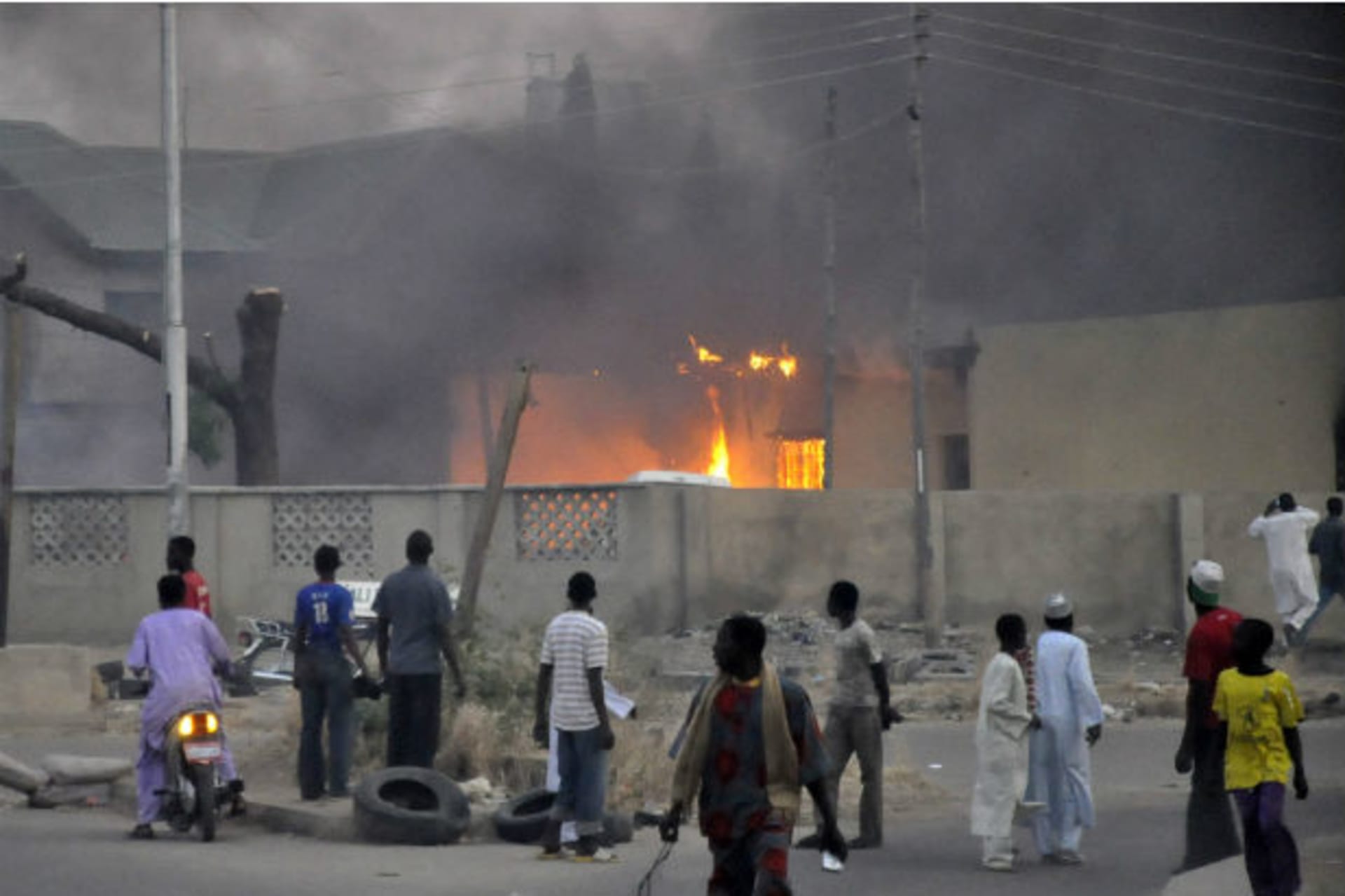 People watch as smoke rises from the police headquarters after it was hit by a blast in Nigeria's northern city of Kano January 20, 2012.