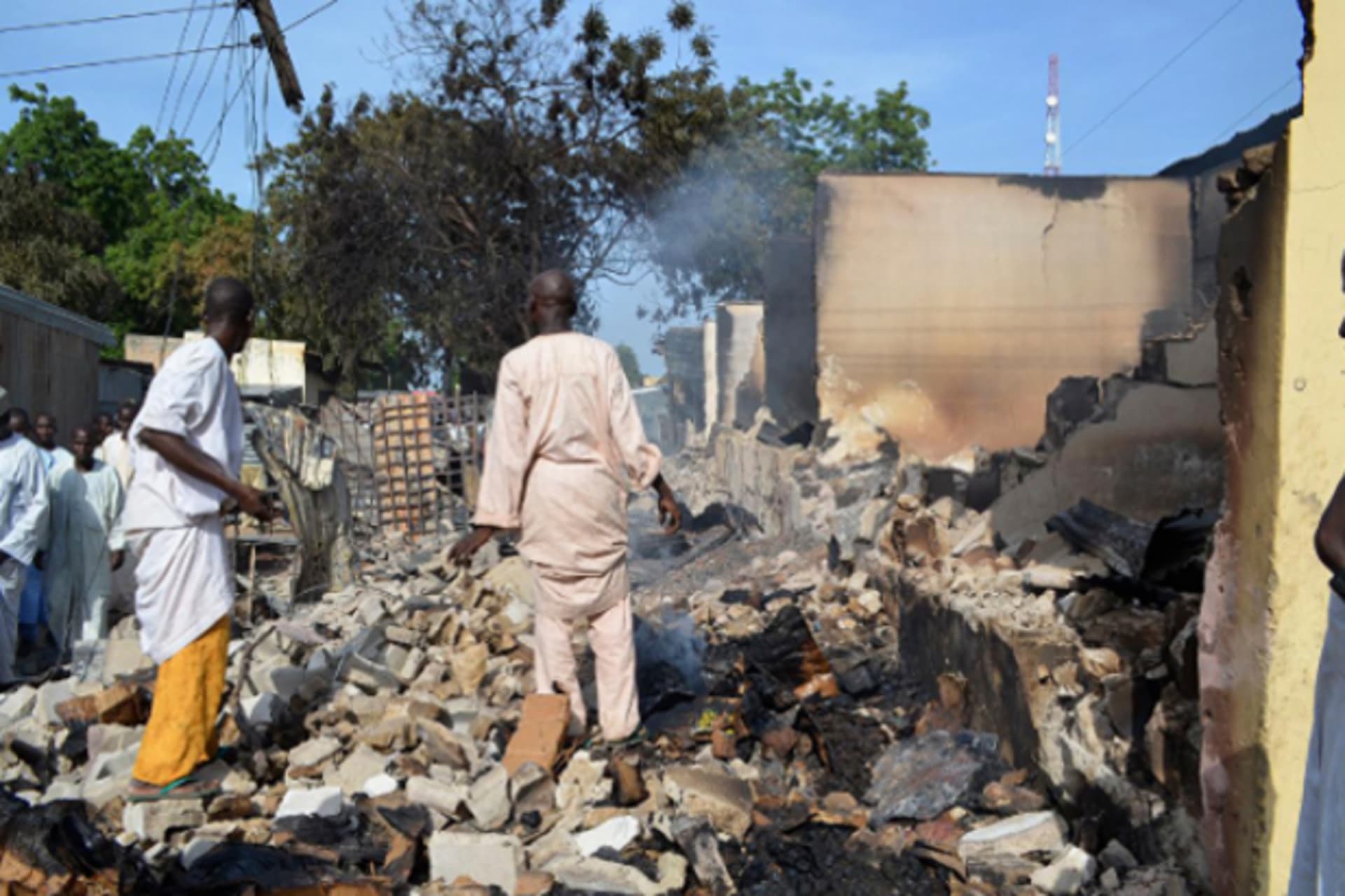 Residents watch as two men walk amidst rubble after Boko Haram militants raided the town of Benisheik, west of Borno State capital Maiduguri September 19, 2013.