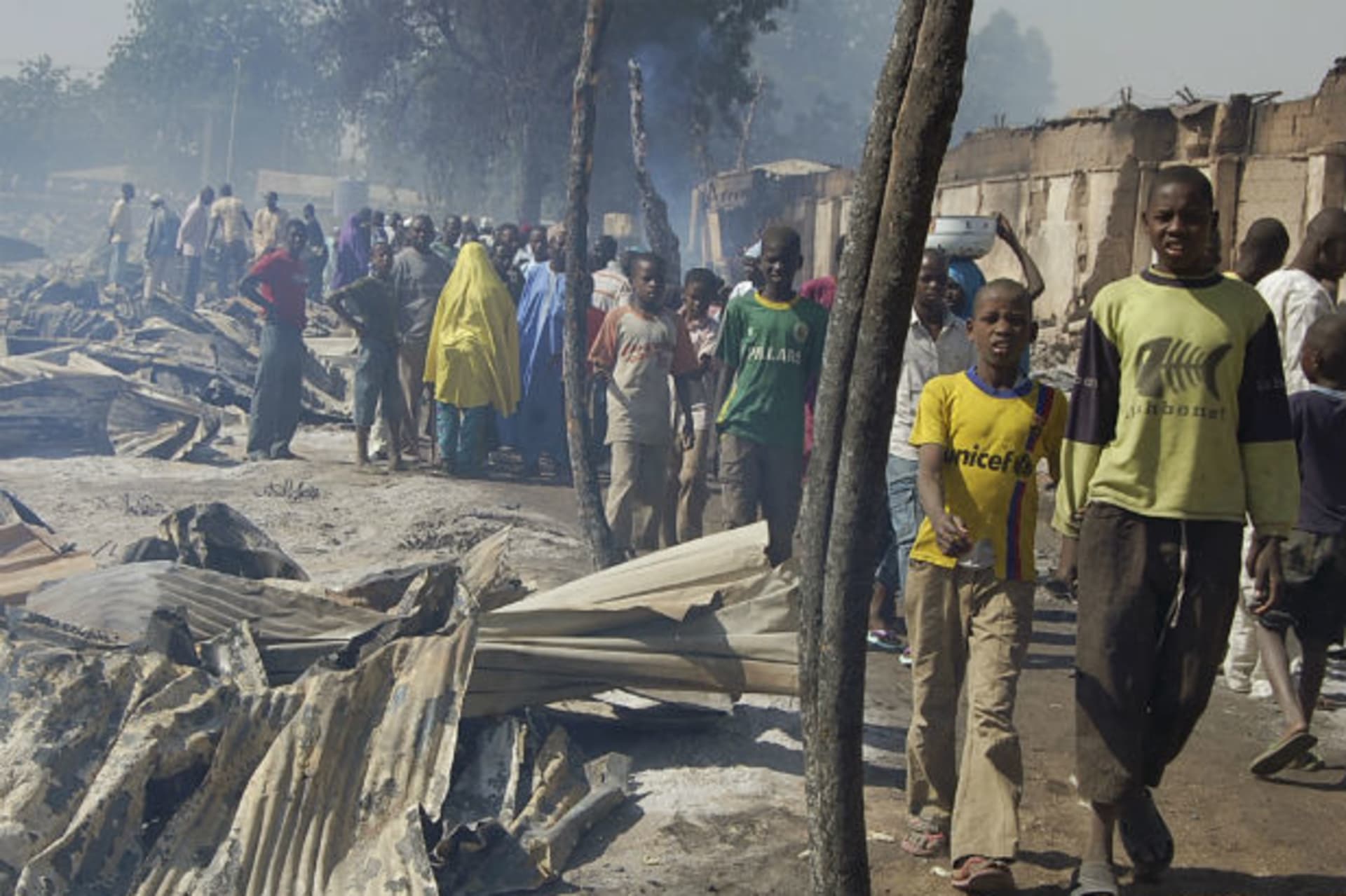 People walk past burnt roofing sheets after a fire razed Gombomru main market in Nigeria's northeastern city of Maiduguri December 24, 2011.