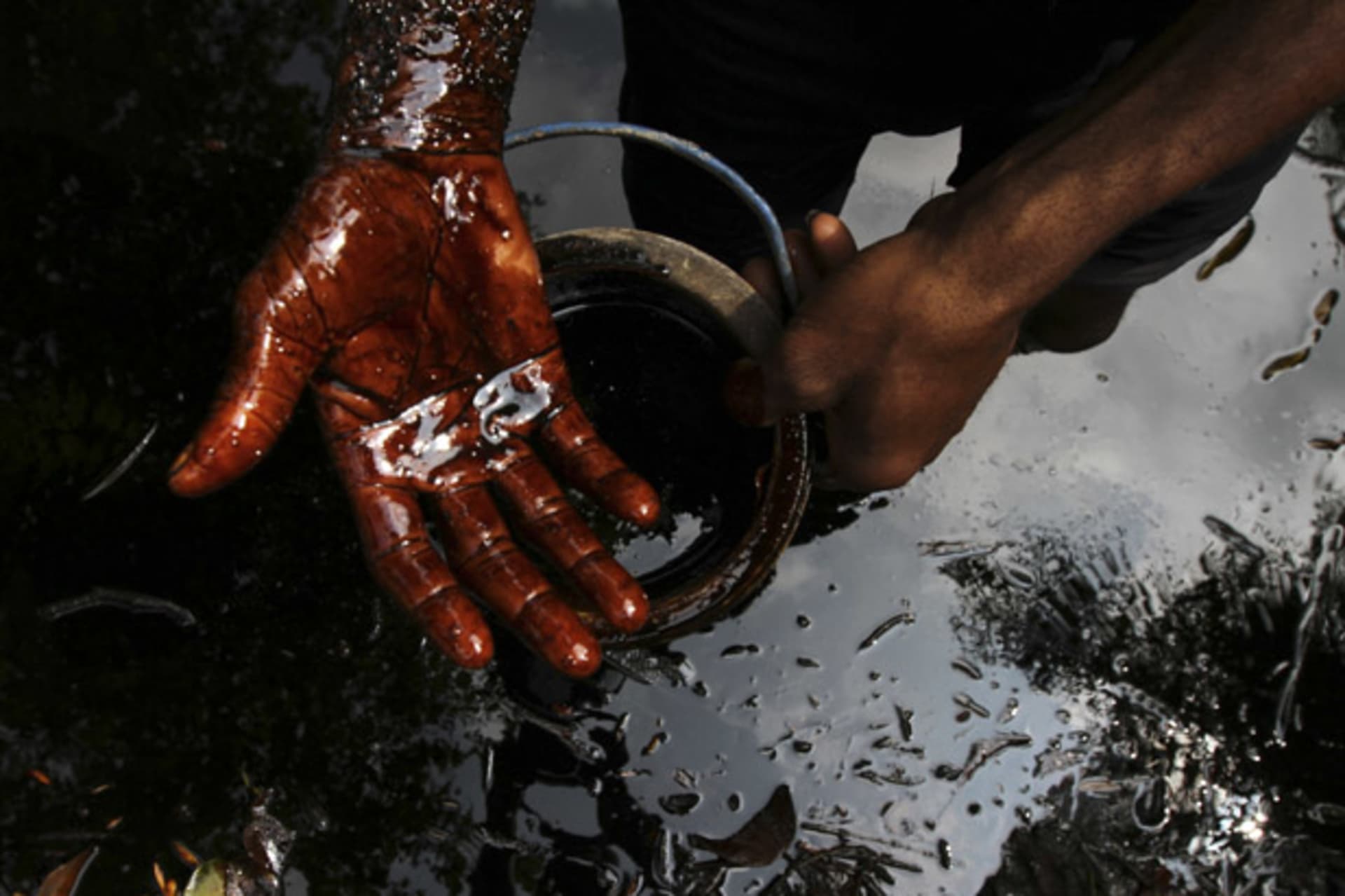 A man samples crude oil at the bank of a polluted river in Bidere community in Ogoniland in Nigeria's delta region