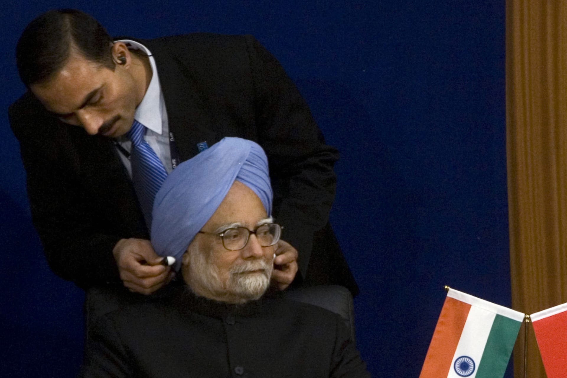 <p>An Indian security personnel assists Indian Prime Minister Manmohan Singh to wear earphones during a speech at the Academy of Social Sciences in Beijing January 15, 2008.</p>

