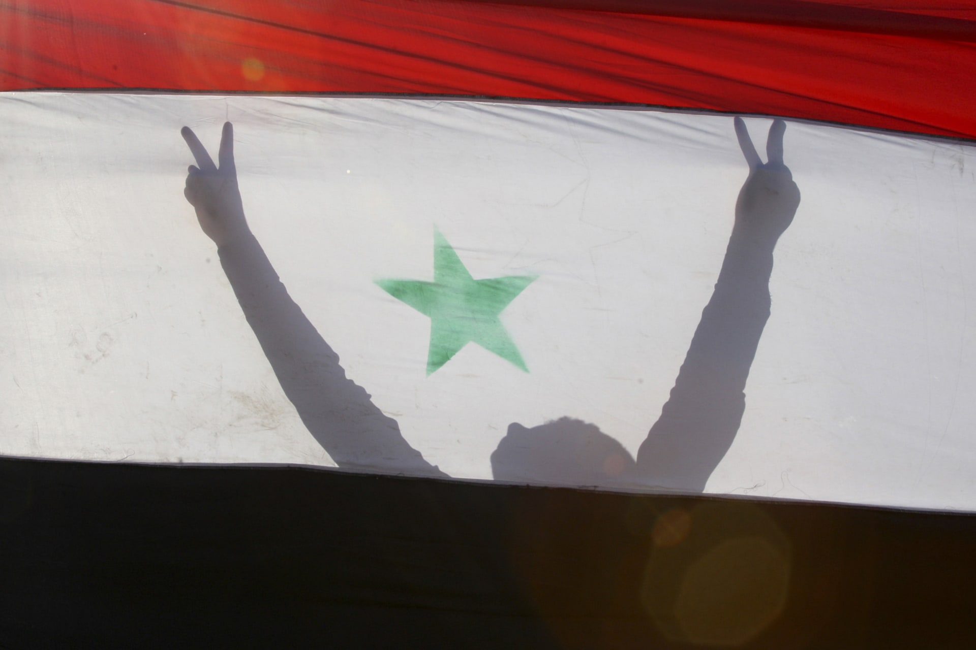 <p>A Syrian protester is silhouetted behind a Syrian flag during a demonstration against President Bashar Al-Assad in front of the Syrian embassy in Amman on June 9, 2011.</p>
