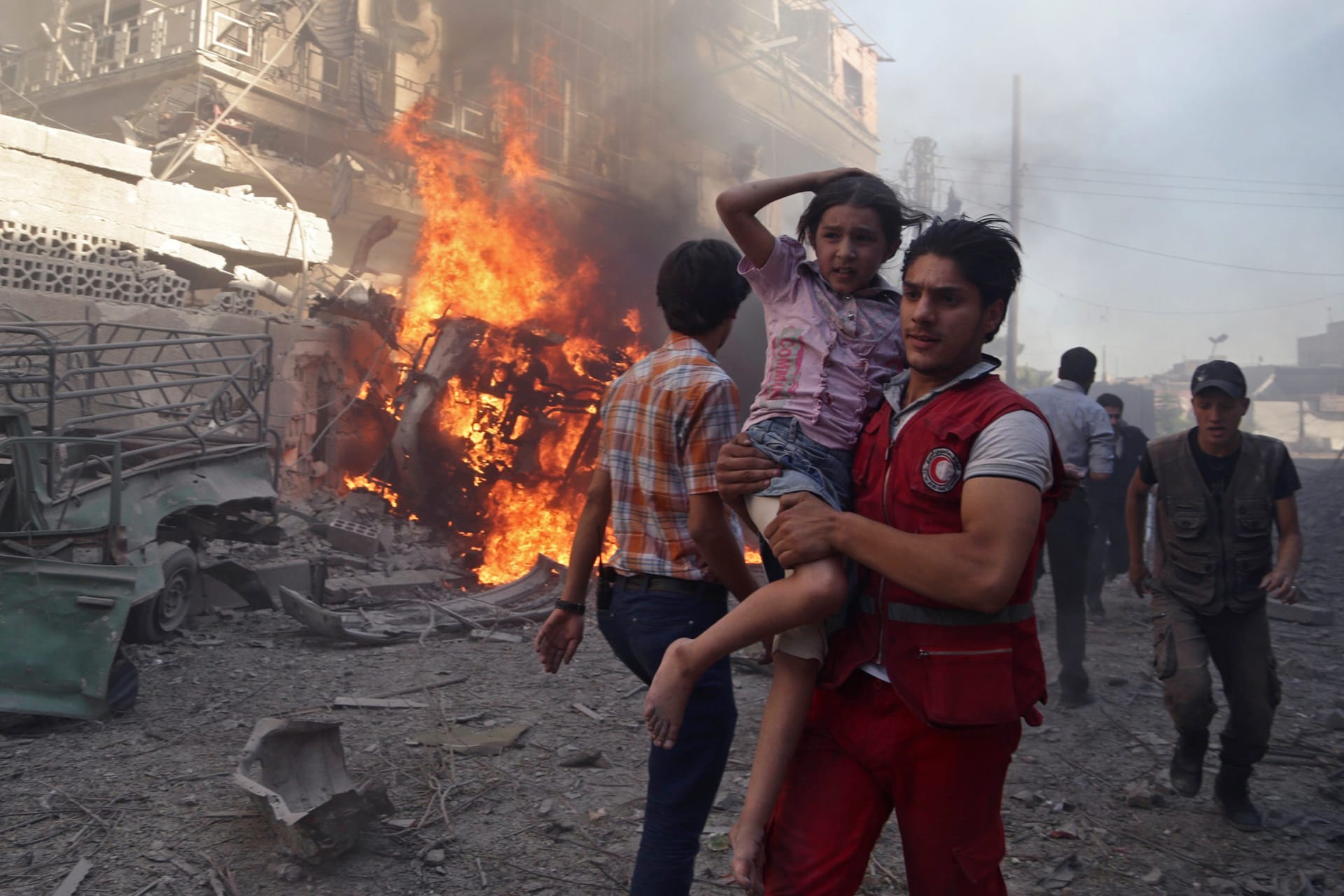 <p>A member of the Syrian Arab Red Crescent carries a girl as they rush away from a site hit by what activists said were airstrikes by forces loyal to Syria’s President Bashar al-Assad in the Douma neighborhood of Damascus, Syria, on August 24, 2015.</p>
