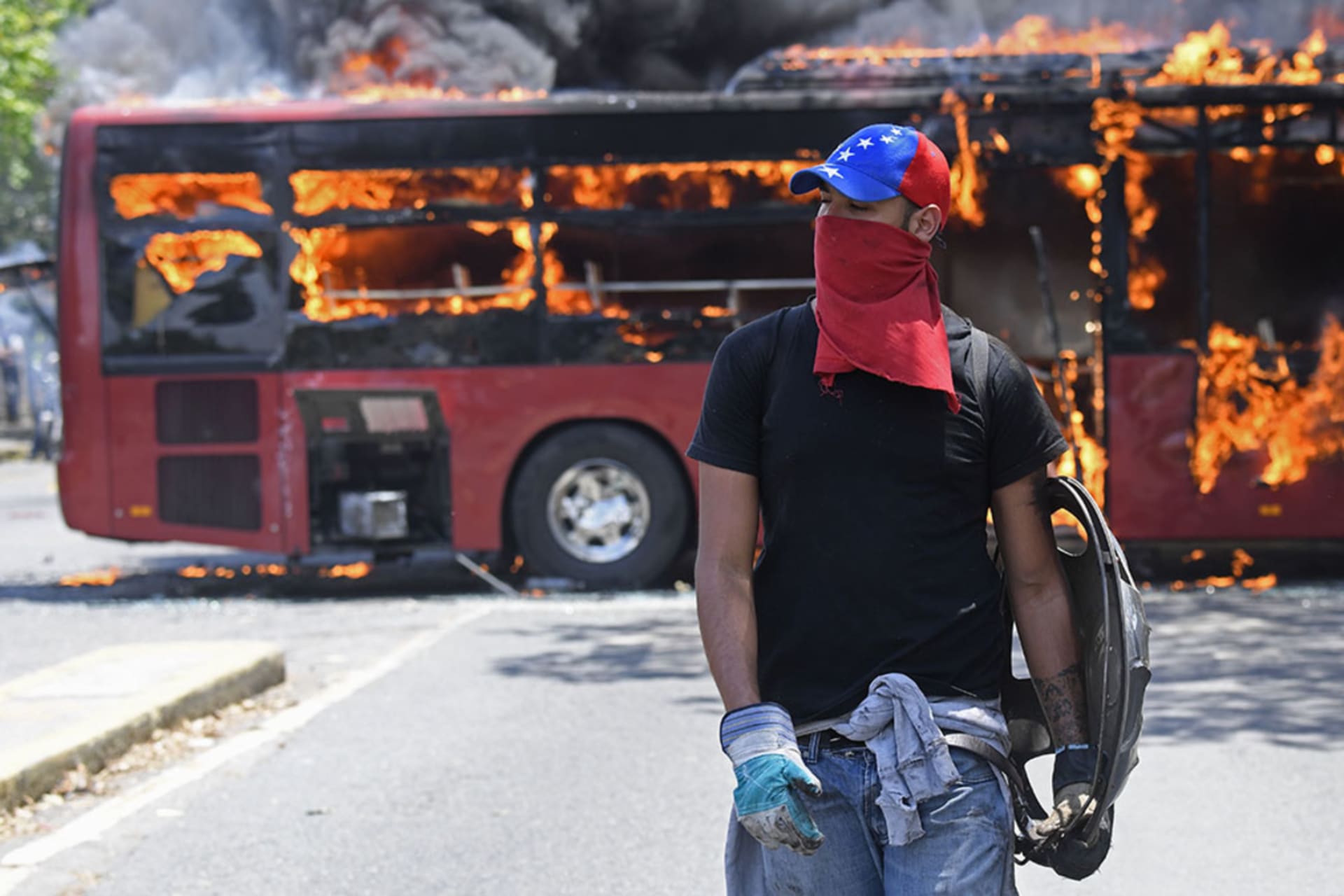 <p>An opposition demonstrator walks near a bus in flames during clashes with soldiers loyal to Venezuelan President Nicolas Maduro in the surroundings of La Carlota military base in Caracas on April 30, 2019.</p>
