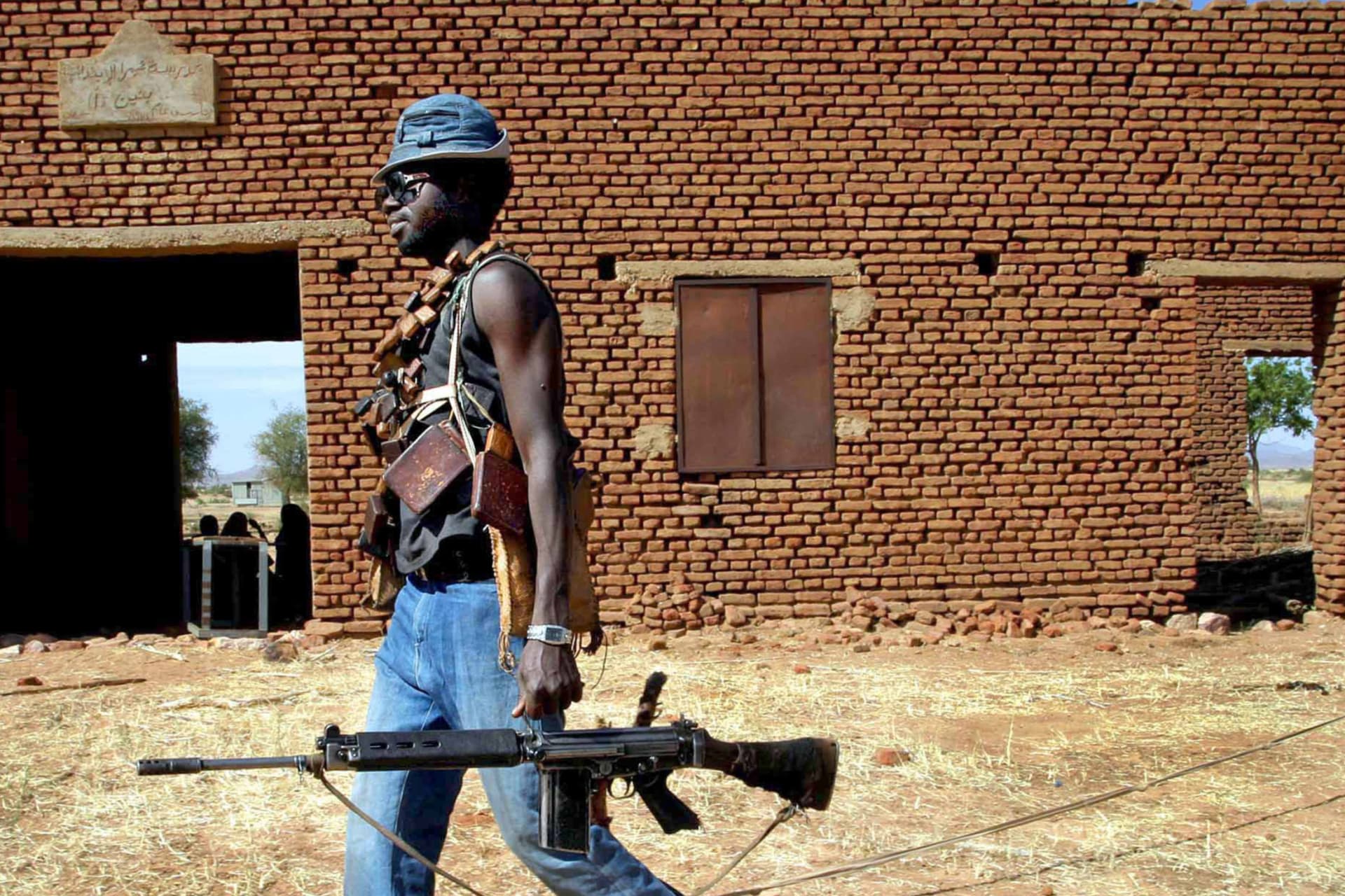 <p>A Sudan Liberation Army (SLA) rebel passes an abandoned building in the desert west of El Fasher, the capital of North Darfur state, on November 8, 2004.</p>
