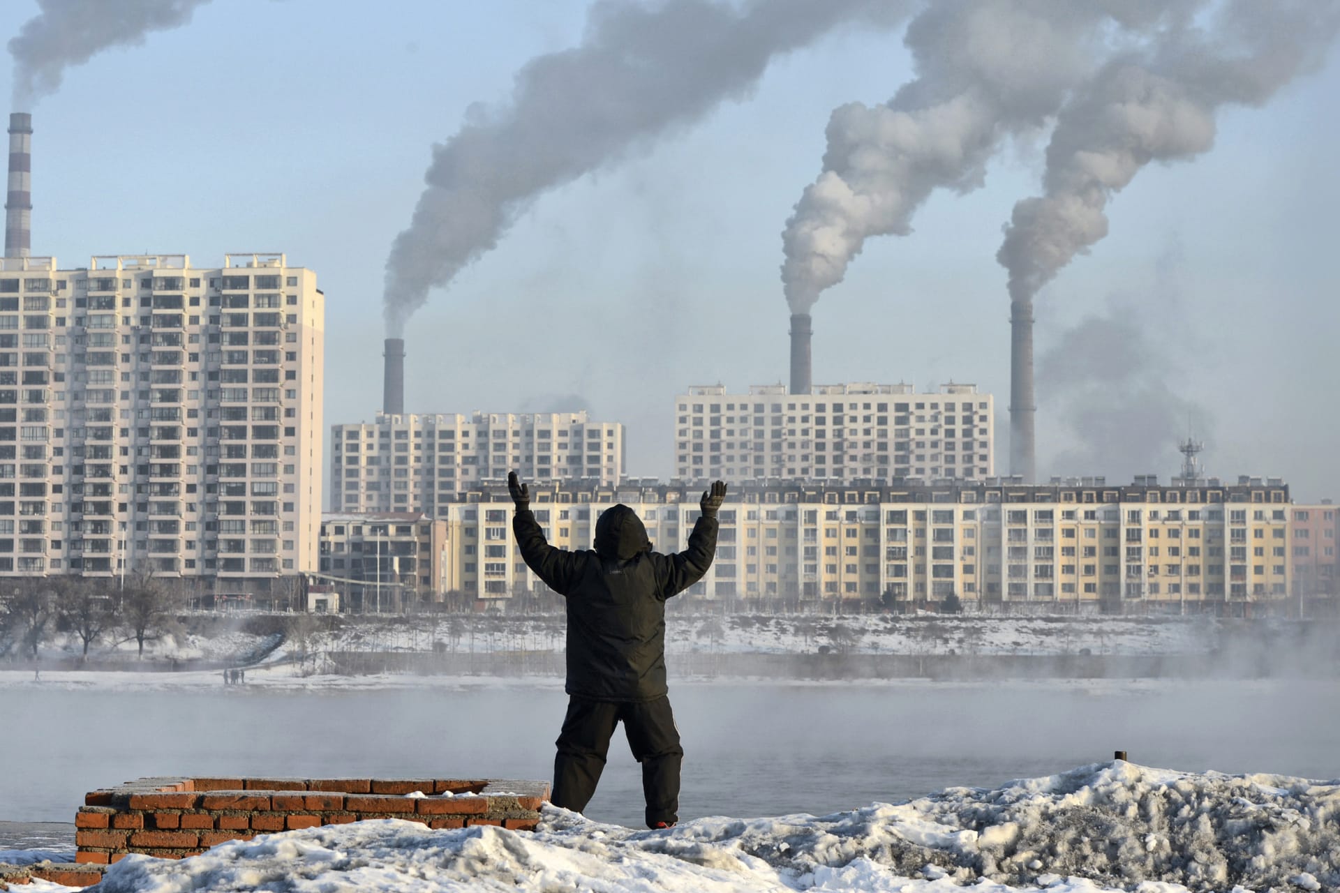 <p>An elderly man exercises in the morning as he faces chimneys emitting smoke behind buildings across the Songhua river in Jilin, Jilin province on February 24, 2013.</p>
