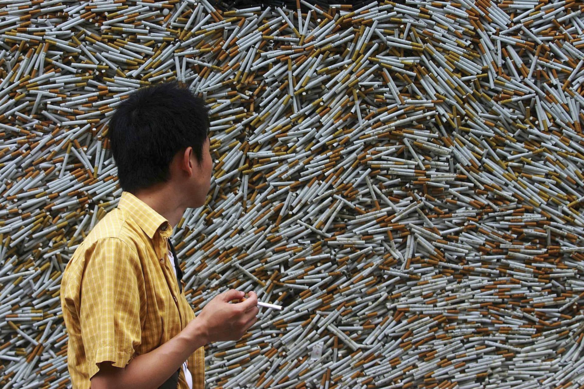 <p>A man smokes his cigarette as he walks past a new art display of a glass container with 10,000 cigarettes in Xiamen, in southeast China’s Fujian province, on May 30, 2007, ahead of the World No Tobacco Day.</p>
