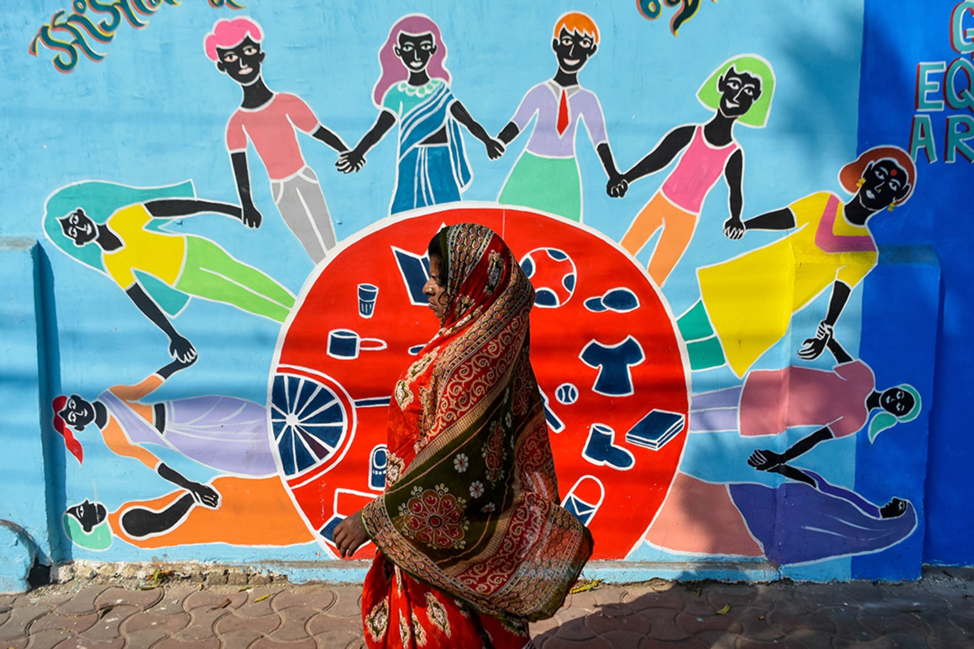 <p>A woman walks past a mural in Kolkata, India, that shows women and girls of various backgrounds holding hands</p>
