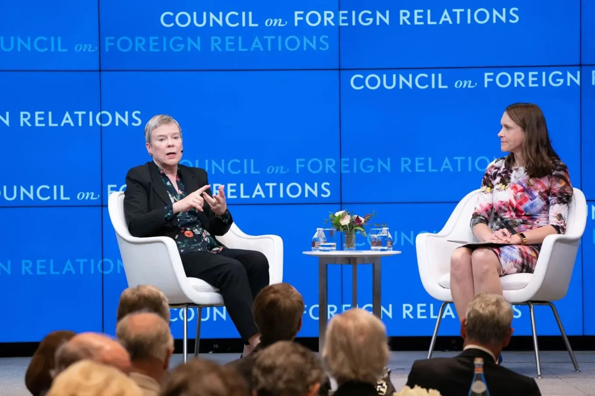 Two people sitting on a stage with a blue background.